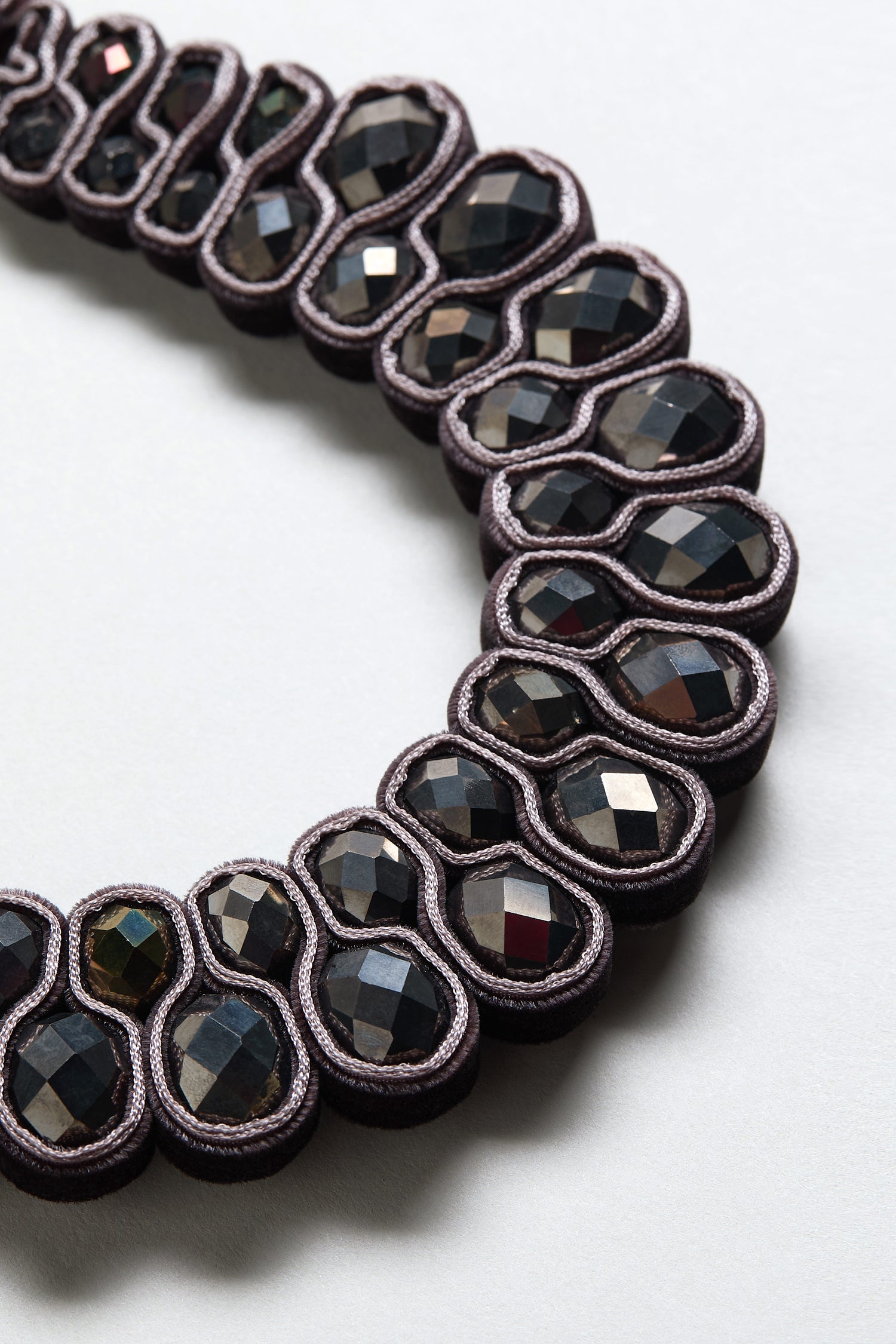 Close-up of the Velvet Ribbon Statement Necklace, featuring dark faceted oval stones set in paired loops on a light background.