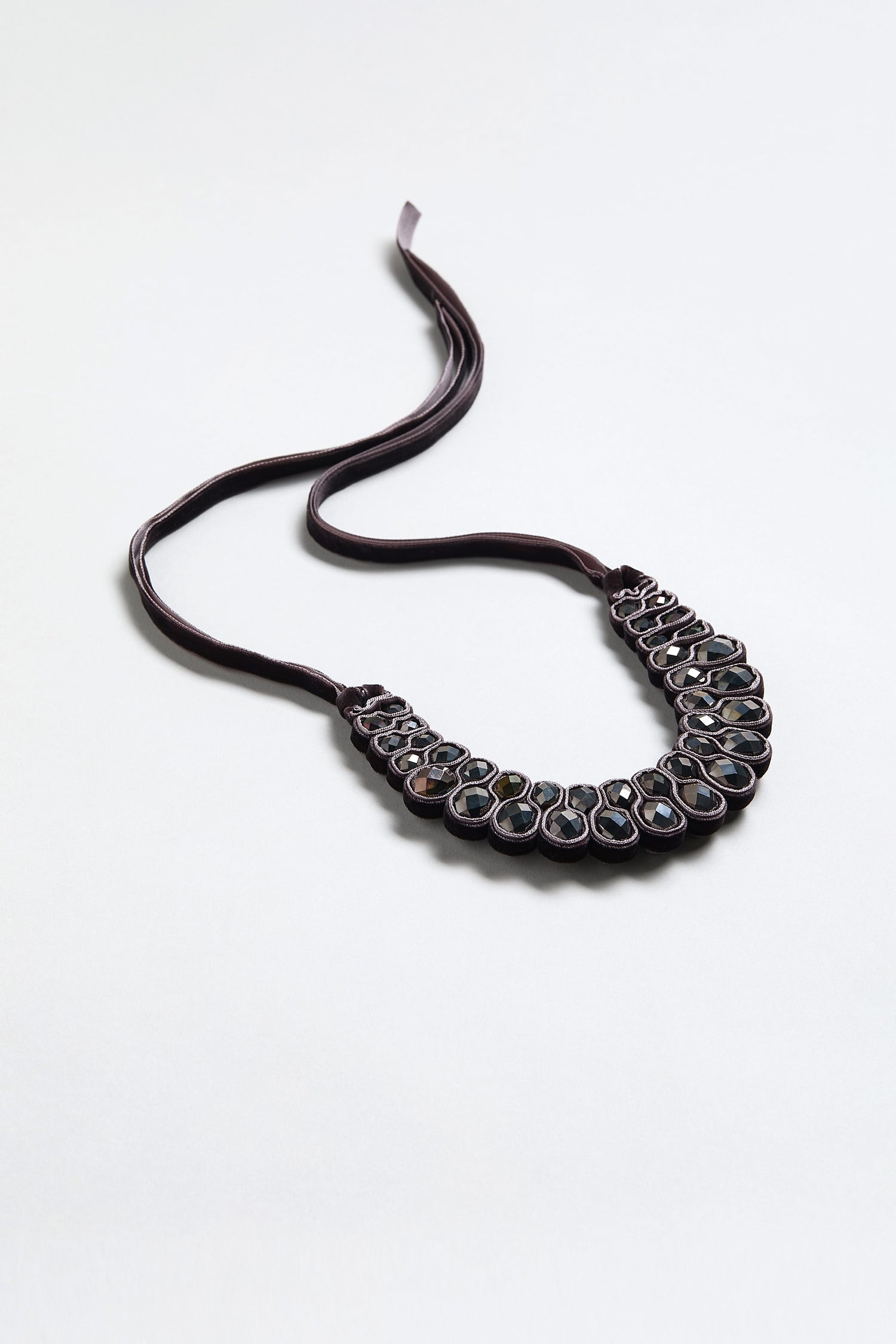 The Velvet Ribbon Statement Necklace features a dark velvet collar and multiple oval-shaped stones in a decorative pattern, shown on a plain light surface.