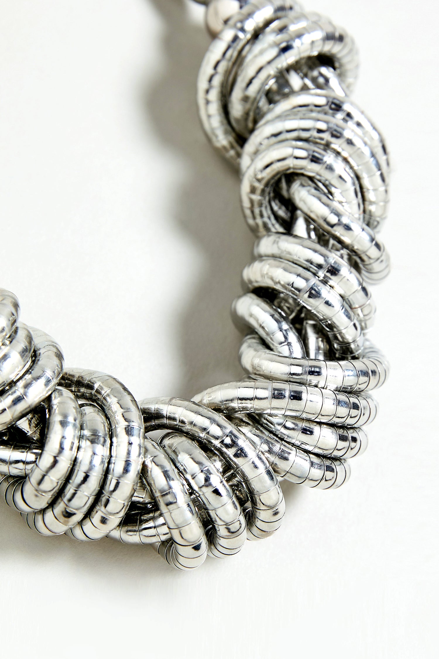 Close-up of the Woven Silver Necklace, featuring multiple shiny, interlocked rings on a light background.