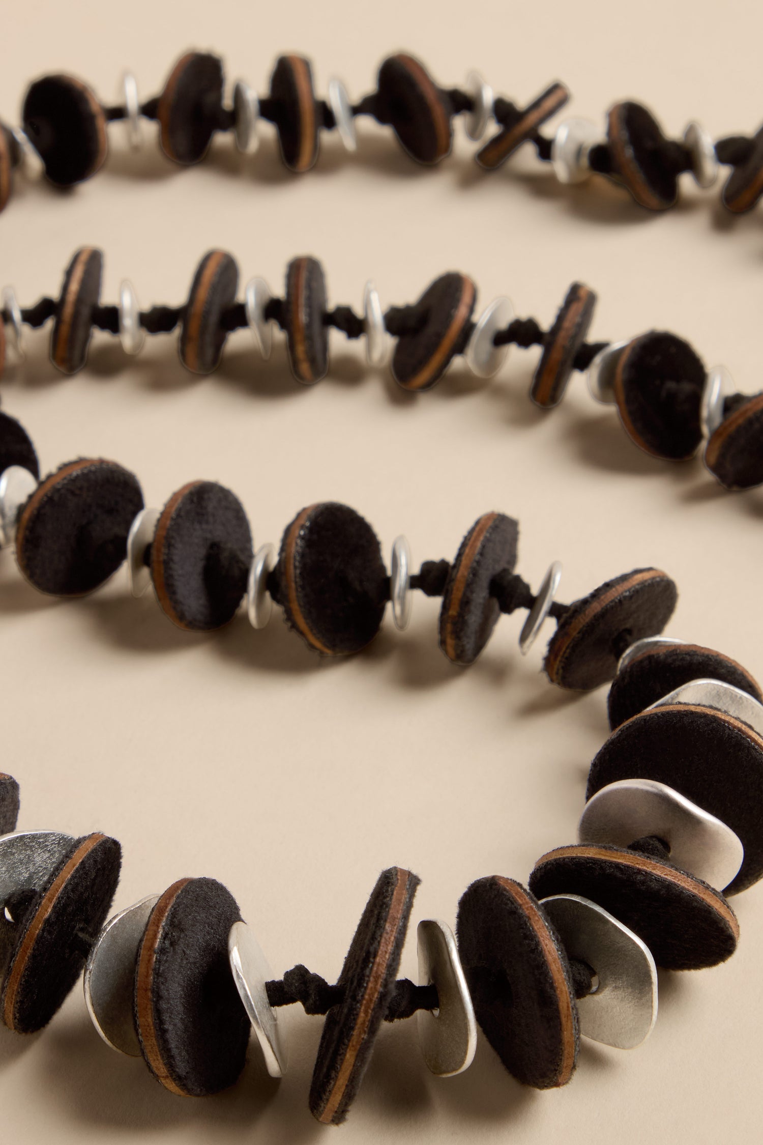 Velvet Detail Disc Necklace consisting of a long strand of alternating black velvet discs and silver-tone metal rings threaded onto a black cord.