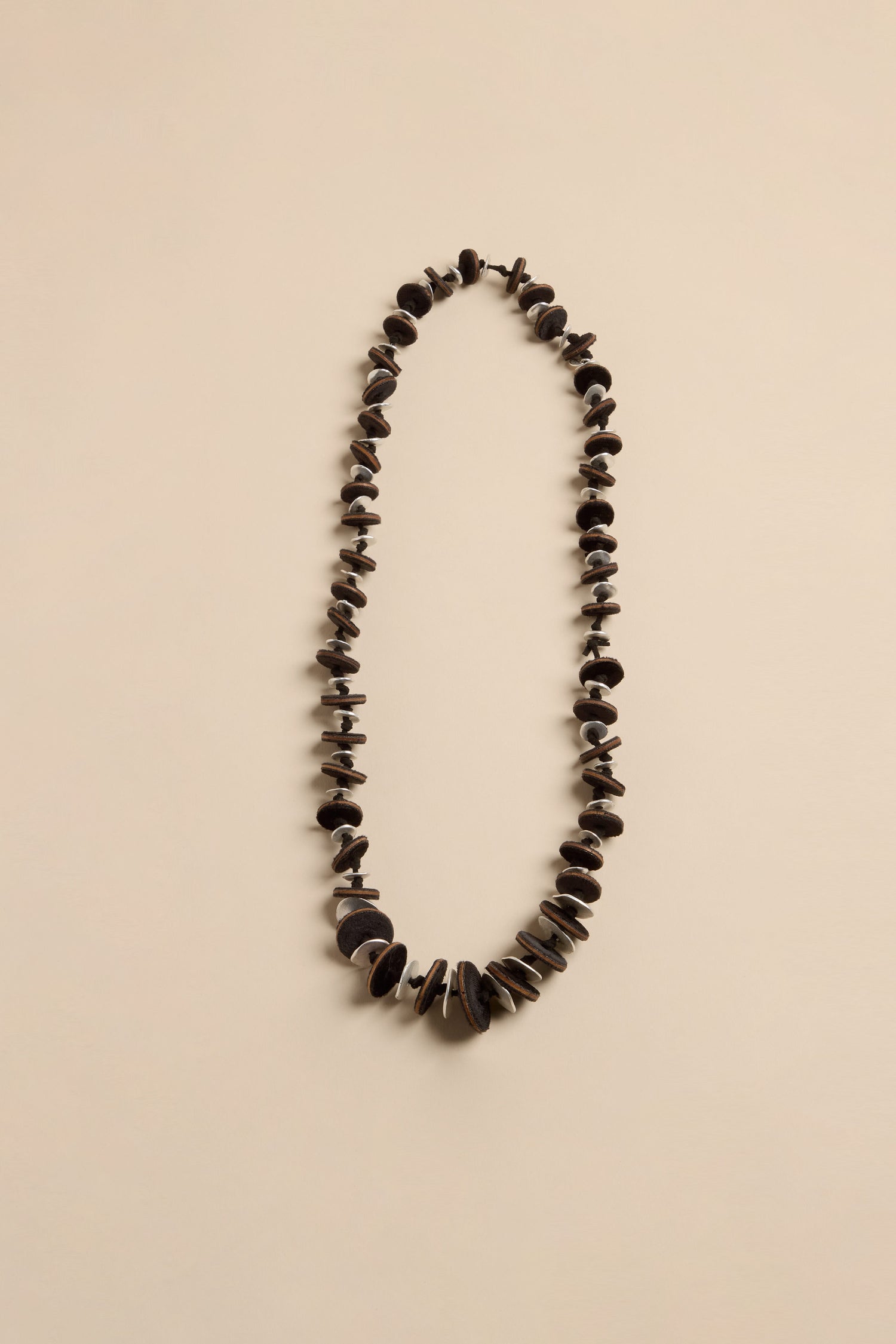 Velvet Detail Disc Necklace consisting of a long cord with alternating small brown circular discs and larger dark brown textured velvet discs.