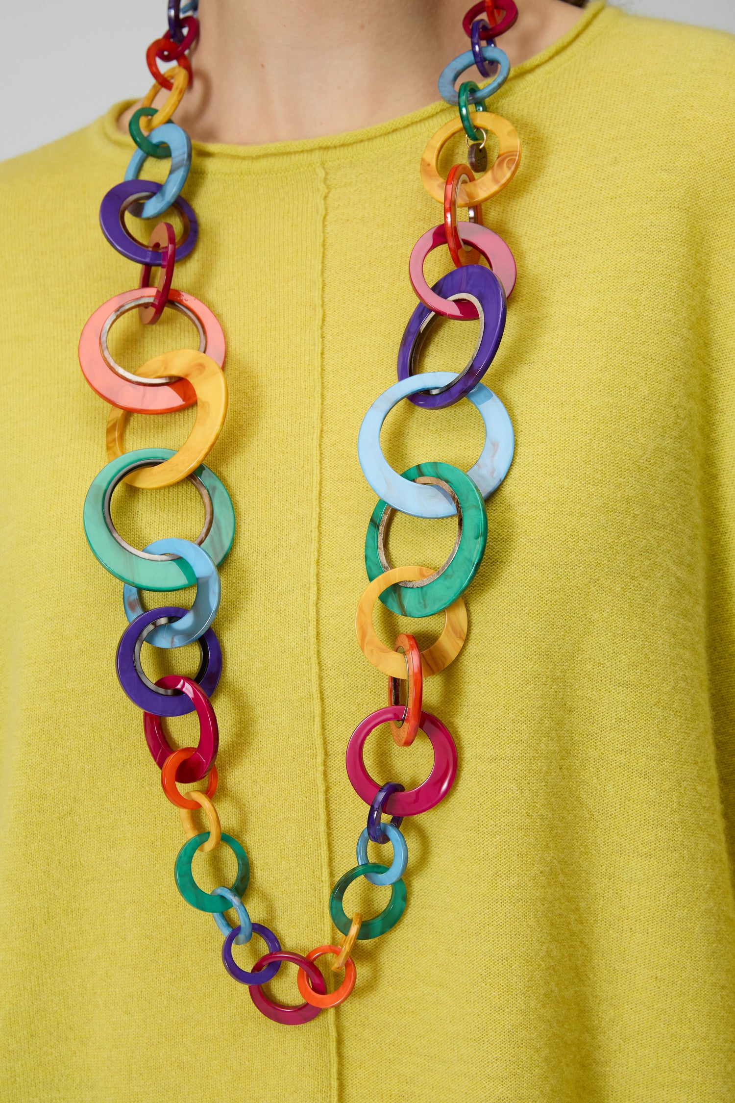 A person wears a yellow textured top and the Rainbow Resin Hoops Necklace, featuring large, colorful interlocking rings for a bold, sculptural statement look.