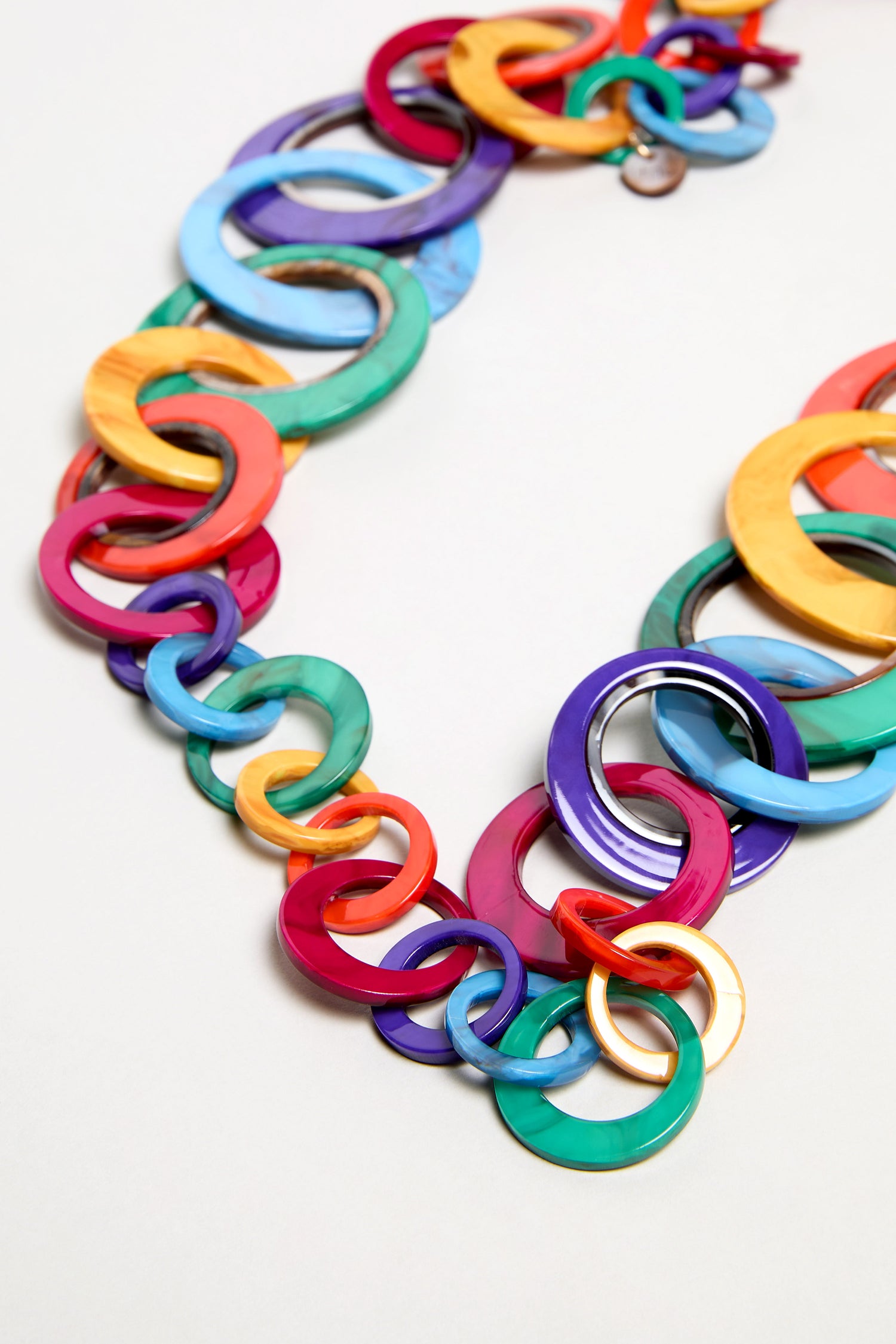 A close-up of the Rainbow Resin Hoops Necklace, showcasing large interlocking resin rings in bright colors on a pale background. This bold, sculptural accessory instantly elevates any outfit.