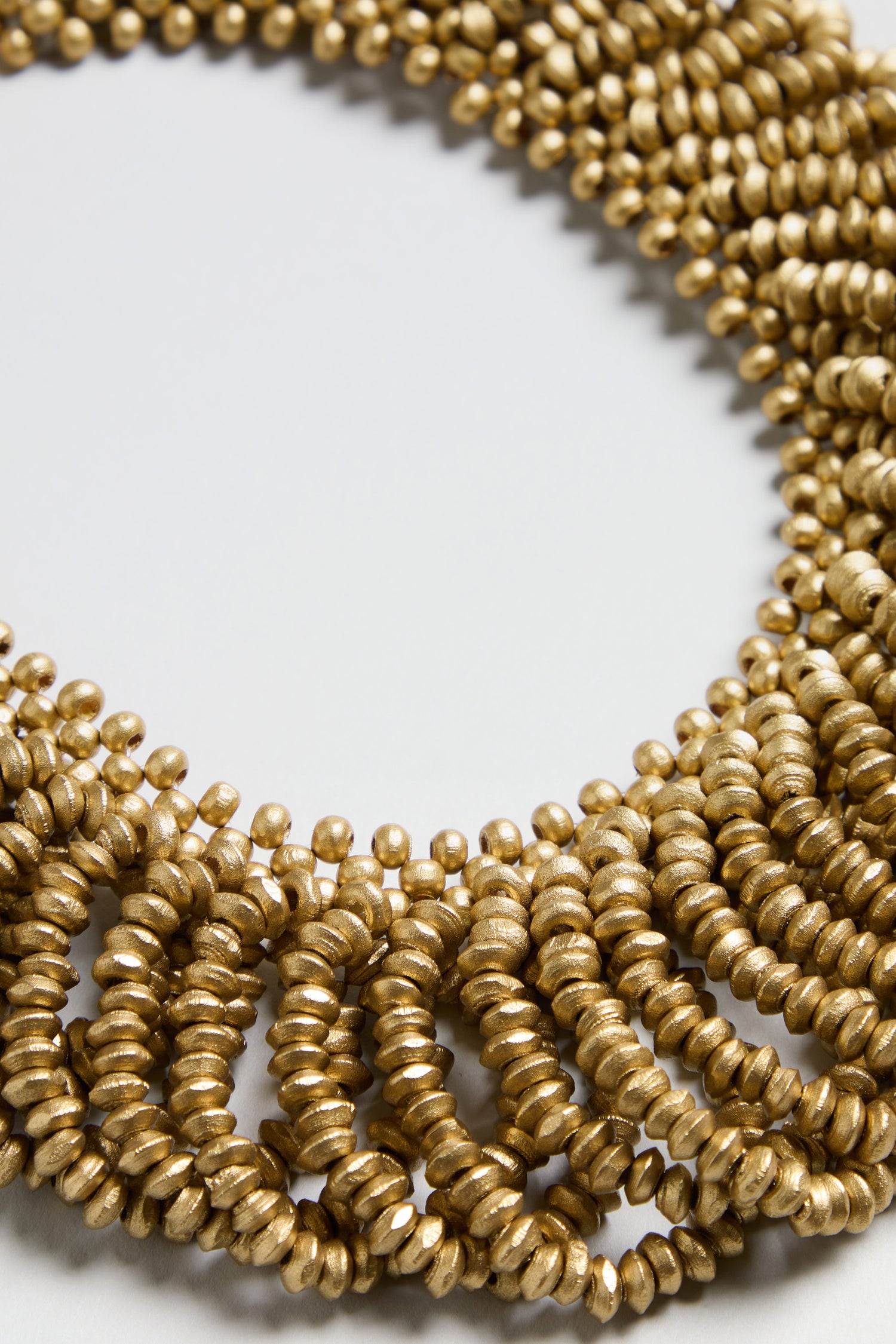 A close-up of the Gold Beaded Collar Necklace, displayed in overlapping loops on a white surface.