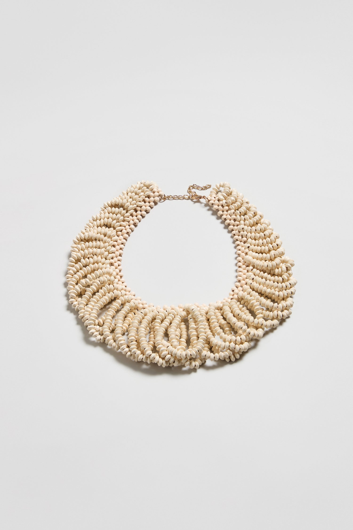 The Natural Beaded Collar Necklace features multiple strands of small, beige seashells in a circular, layered design with a secure clasp closure.