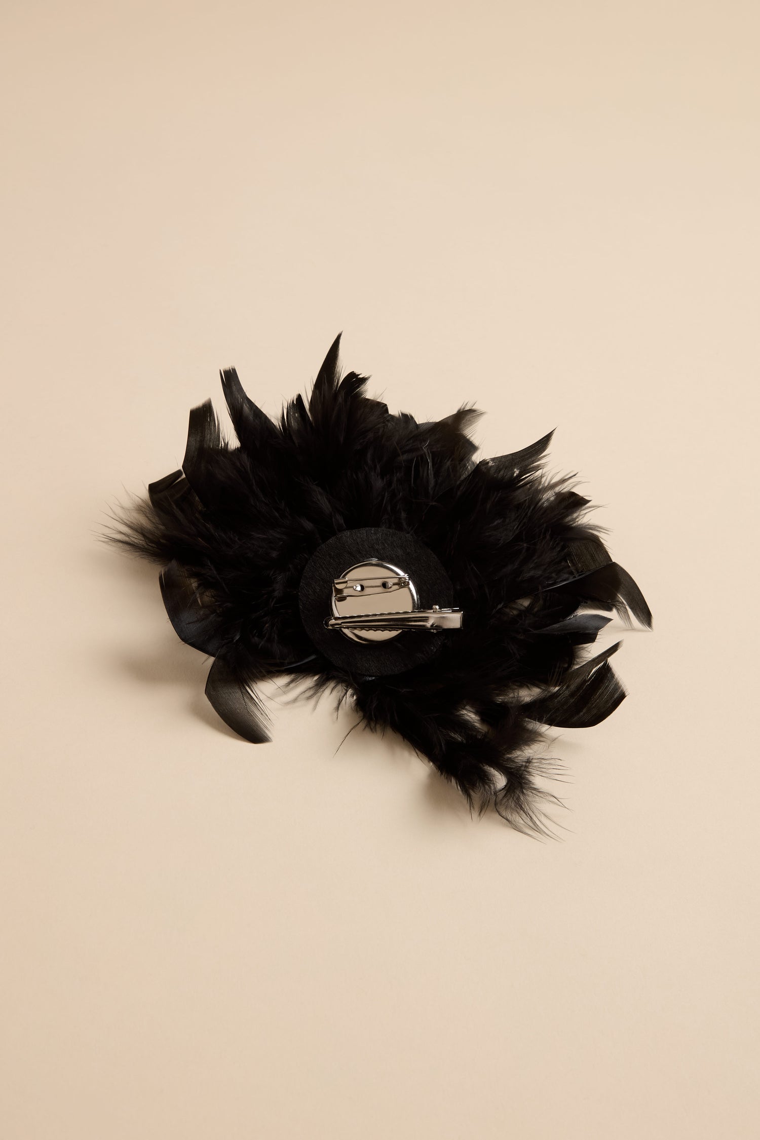 Back view of a black Feather Corsage, featuring a metal hair clip and pin attachment for use as a versatile statement accessory.