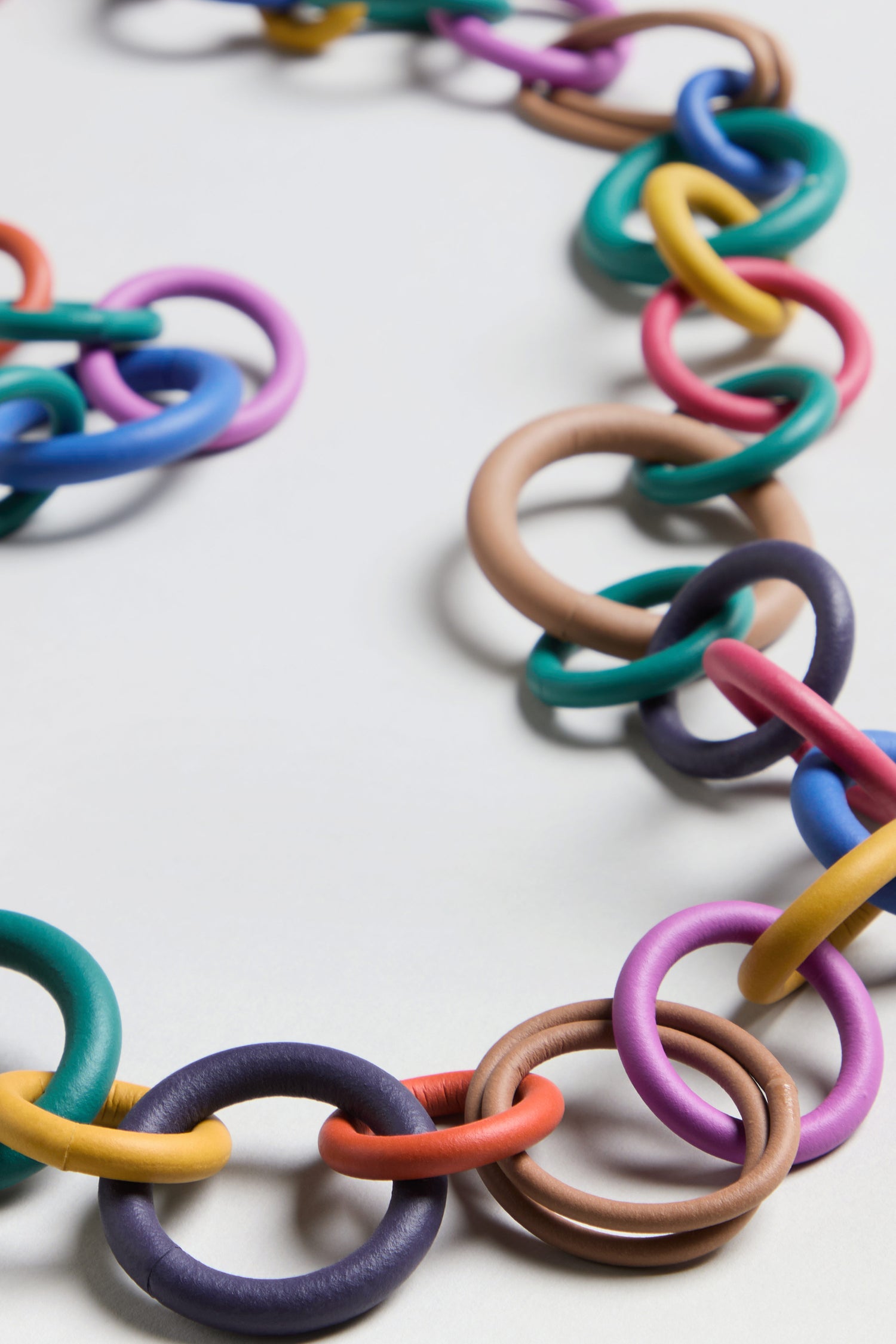 A close-up of the Long Rainbow Hoops Necklace, featuring interlocking colorful rings, displayed on a plain white surface.