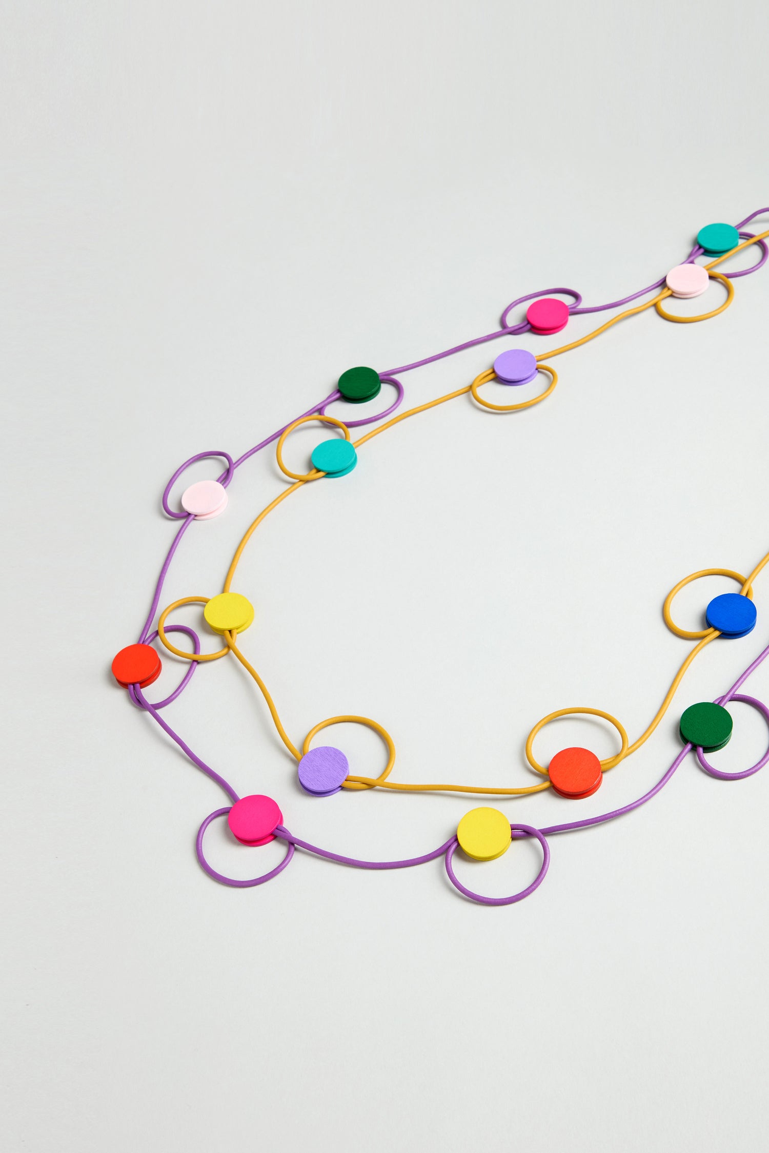 Two Rainbow Circle Hoop Necklaces—one purple, one yellow—feature lightweight circular beads and loops, artfully arranged on a light background for a vibrant display of contemporary jewelry.