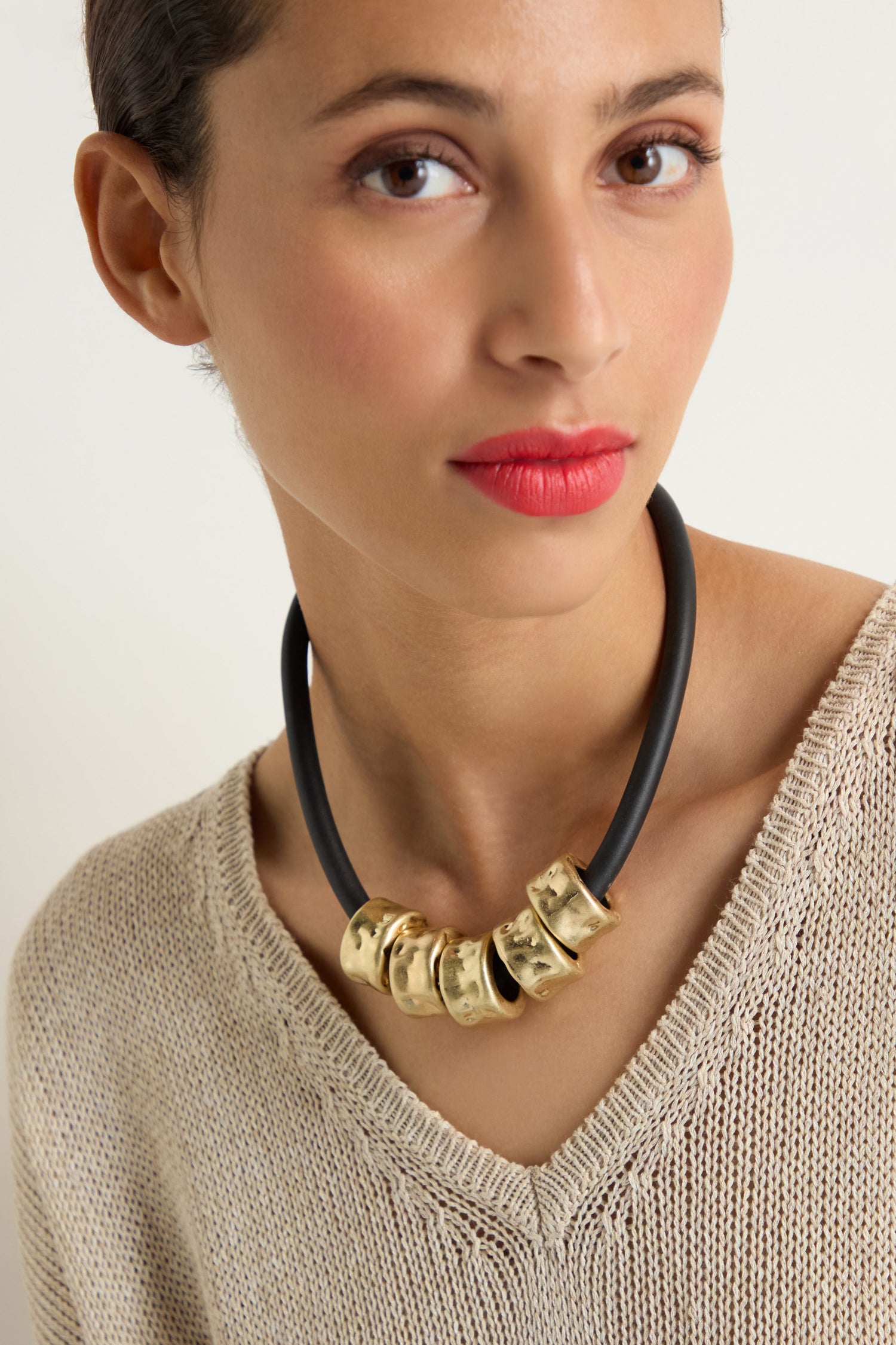 Woman with wavy dark hair wearing a blue top and the Hammered Cylinders Necklace, looking to her left against a plain background.