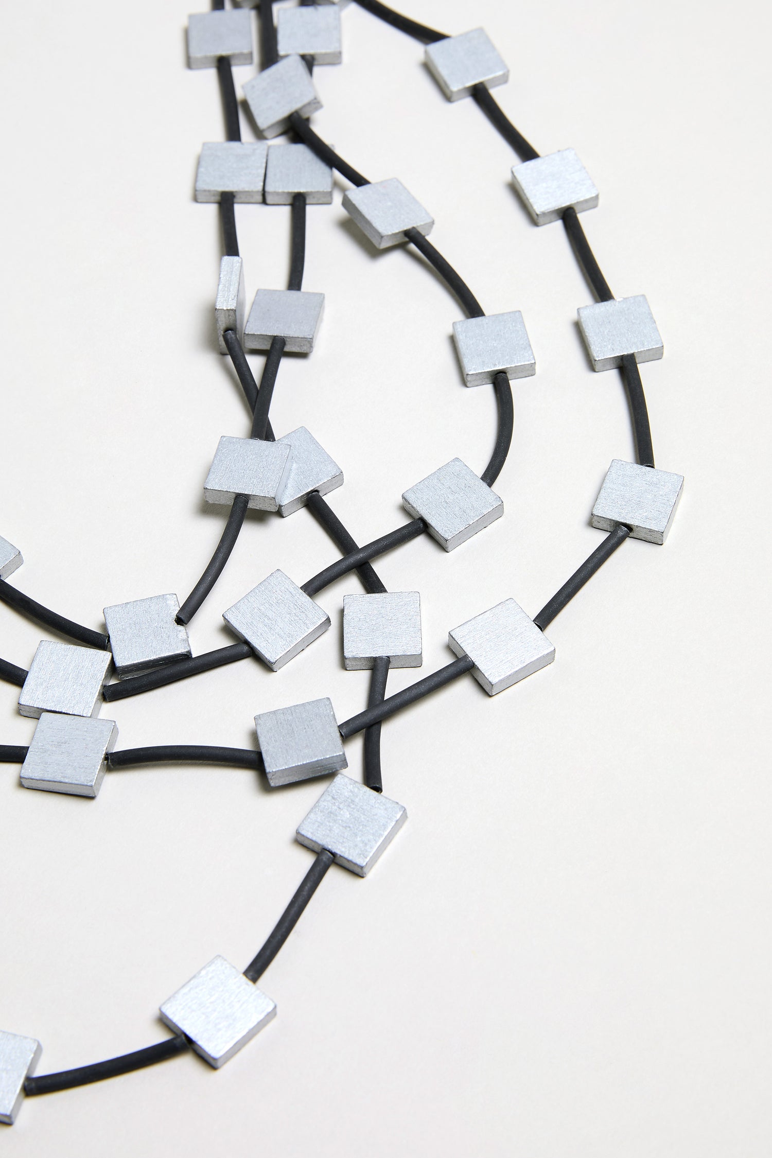 The Cascade Squares Necklace features multiple strands of black beads and silver-tone square accents, beautifully displayed on a light surface.