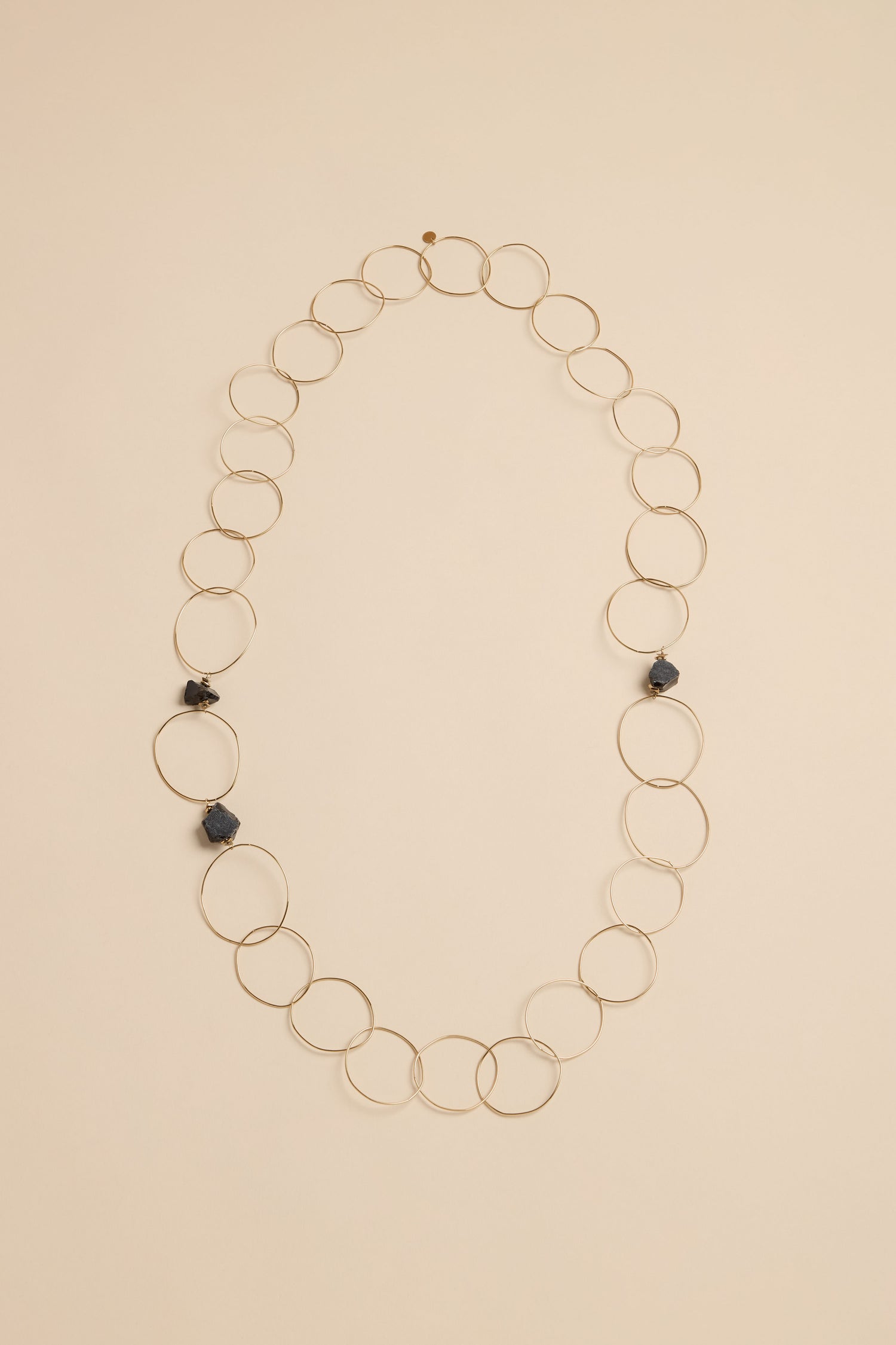Midnight Stone Link Necklace featuring a long chain of thin gold-tone metal rings accented by three dark, irregular stones.
