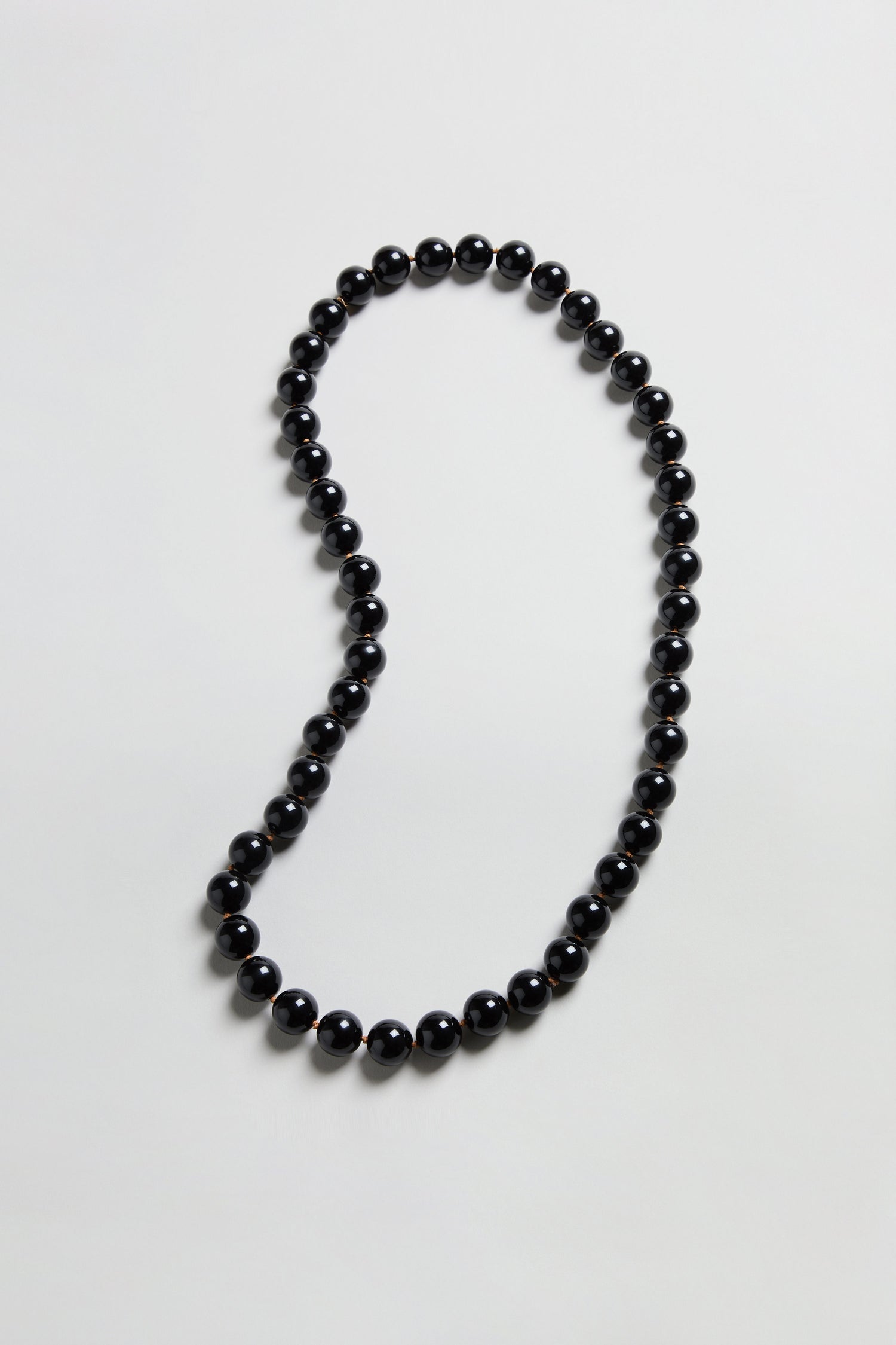 The Long Spheres Necklace features a single strand of round black beads arranged in an irregular loop on a simple, light-colored background.