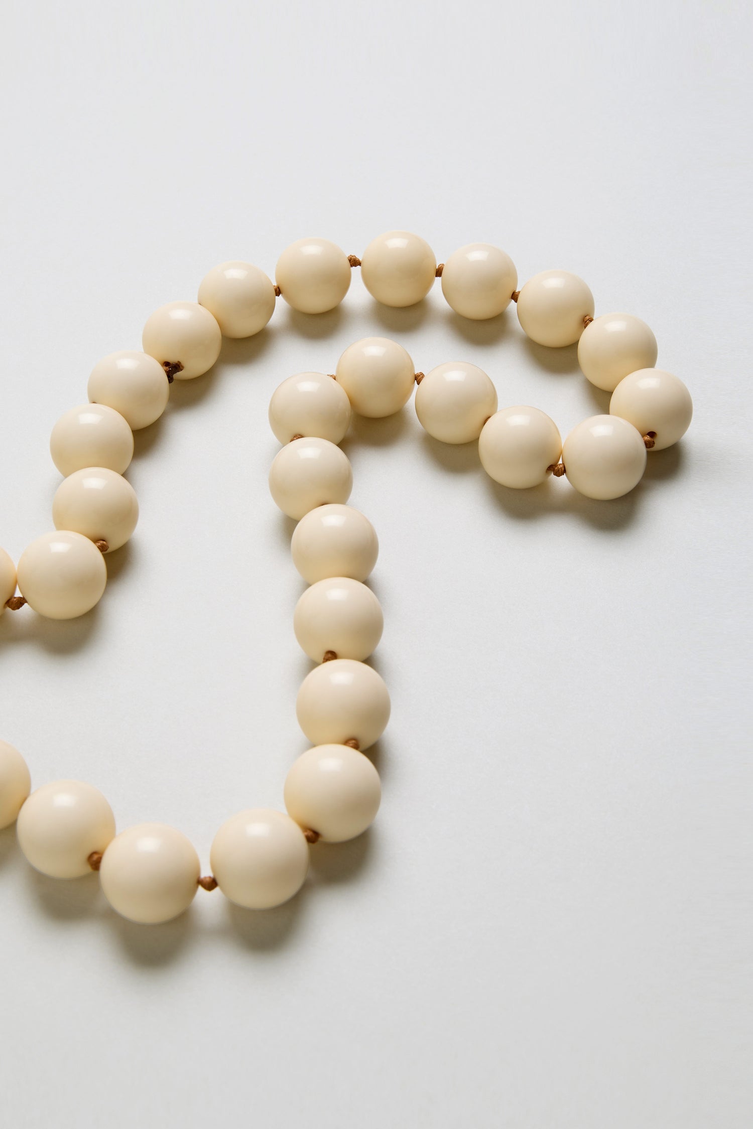 A close-up of the Long Spheres Necklace, showcasing large cream-colored resin sphere beads arranged in a loose curve on a light background.
