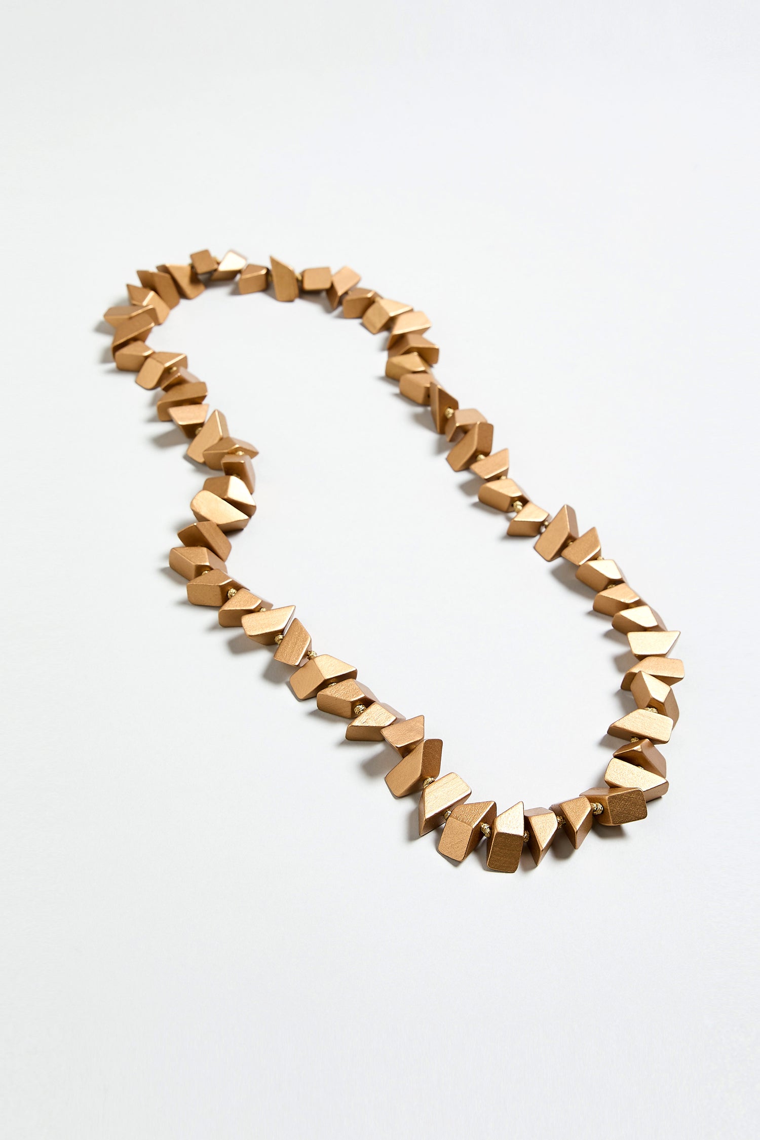 The Long Wooden Metallic Necklace features lightweight, irregular faceted wooden beads with a gold-toned geometric design, arranged in a single strand and displayed on a plain white background.