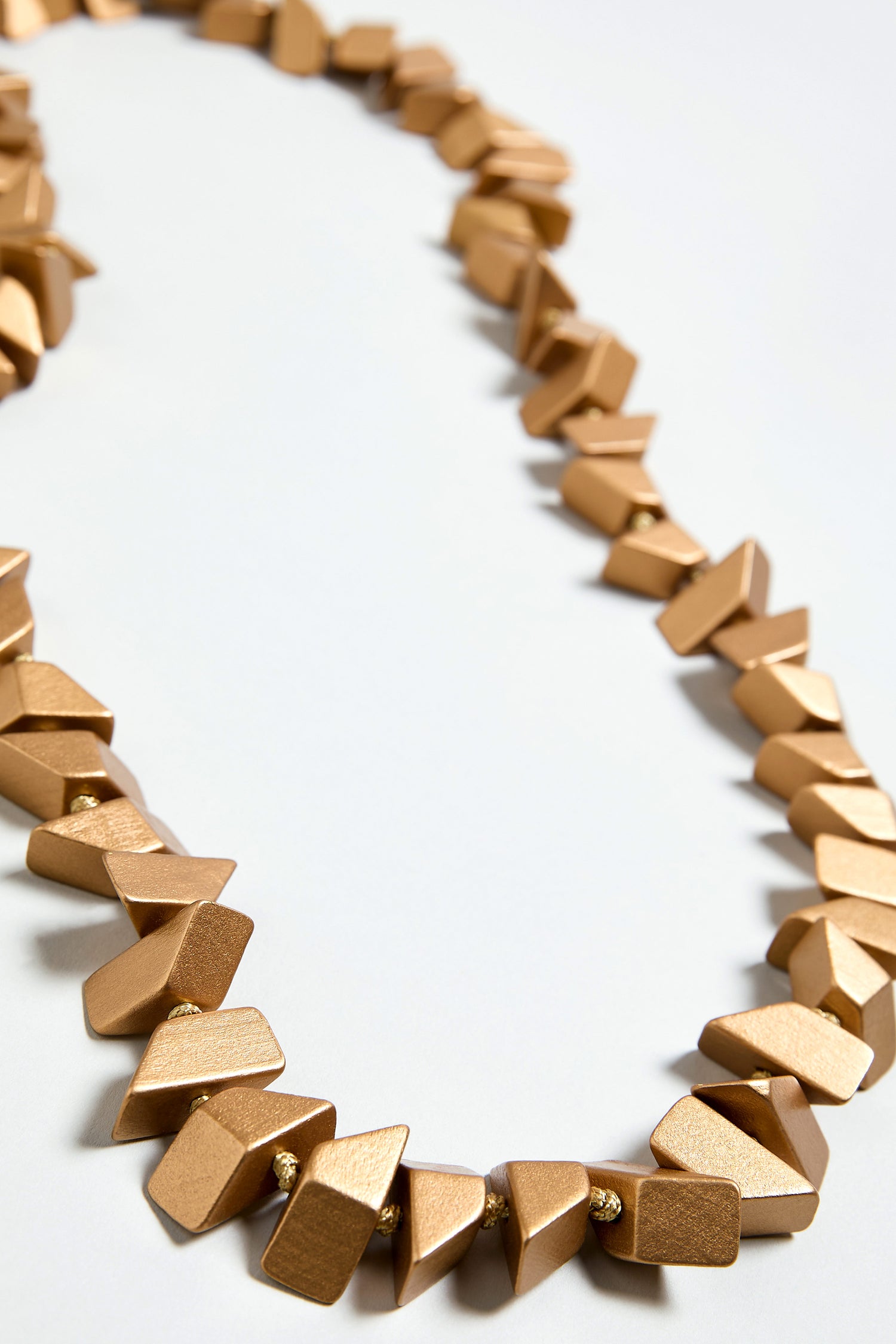 The Long Wooden Metallic Necklace is a gold-toned, lightweight statement piece featuring irregular faceted wooden beads in a single strand.