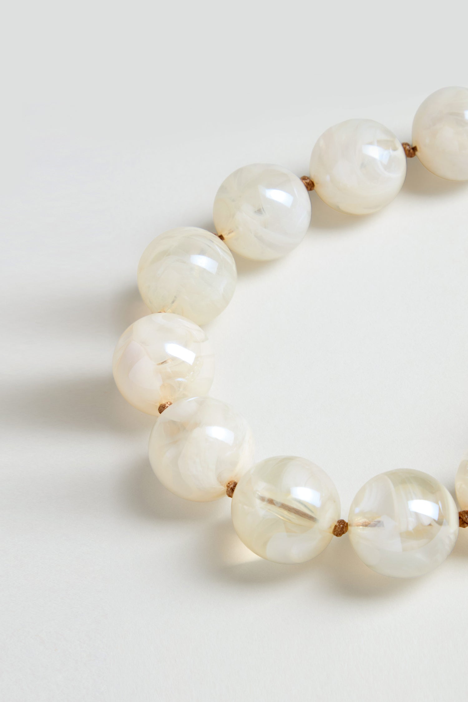 A close-up of the Marble Spheres Necklace, featuring large semi-translucent white marbled beads on a tan cord, displayed against a plain light background.