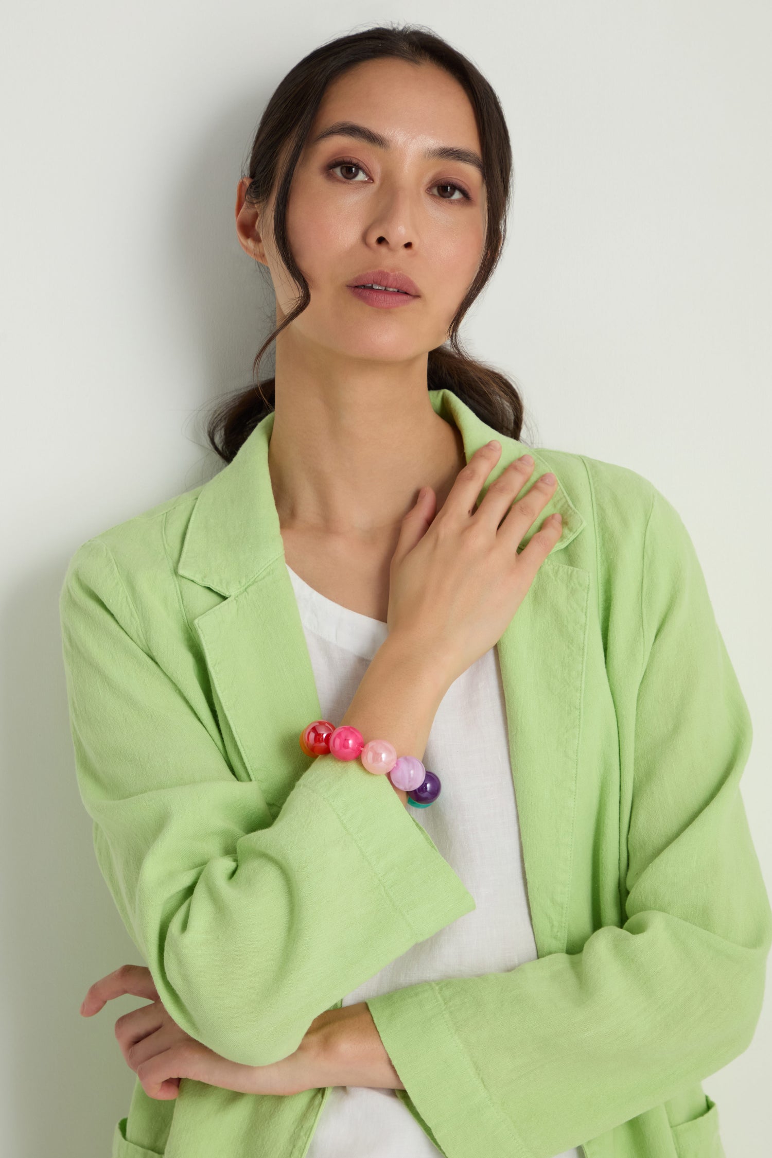 A woman in a light green blazer and white shirt poses with her hand on her chest, showcasing the vibrant Colour Pop Resin Spheres Bracelet.