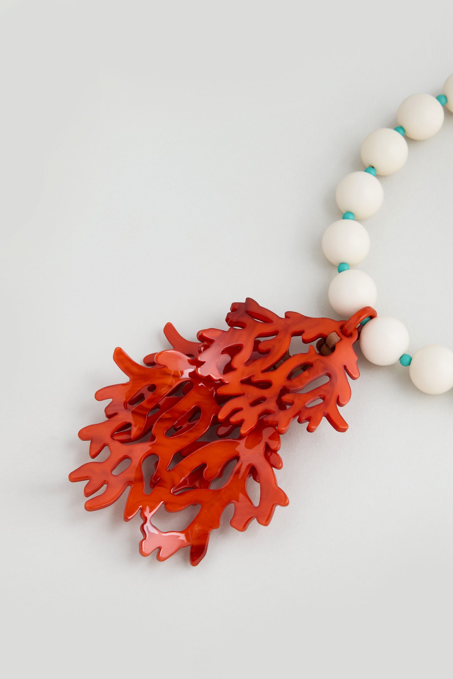 The Coral Resin Short Pendant Necklace features a white beaded strand and a bold, large red coral resin pendant—perfect for making a statement.