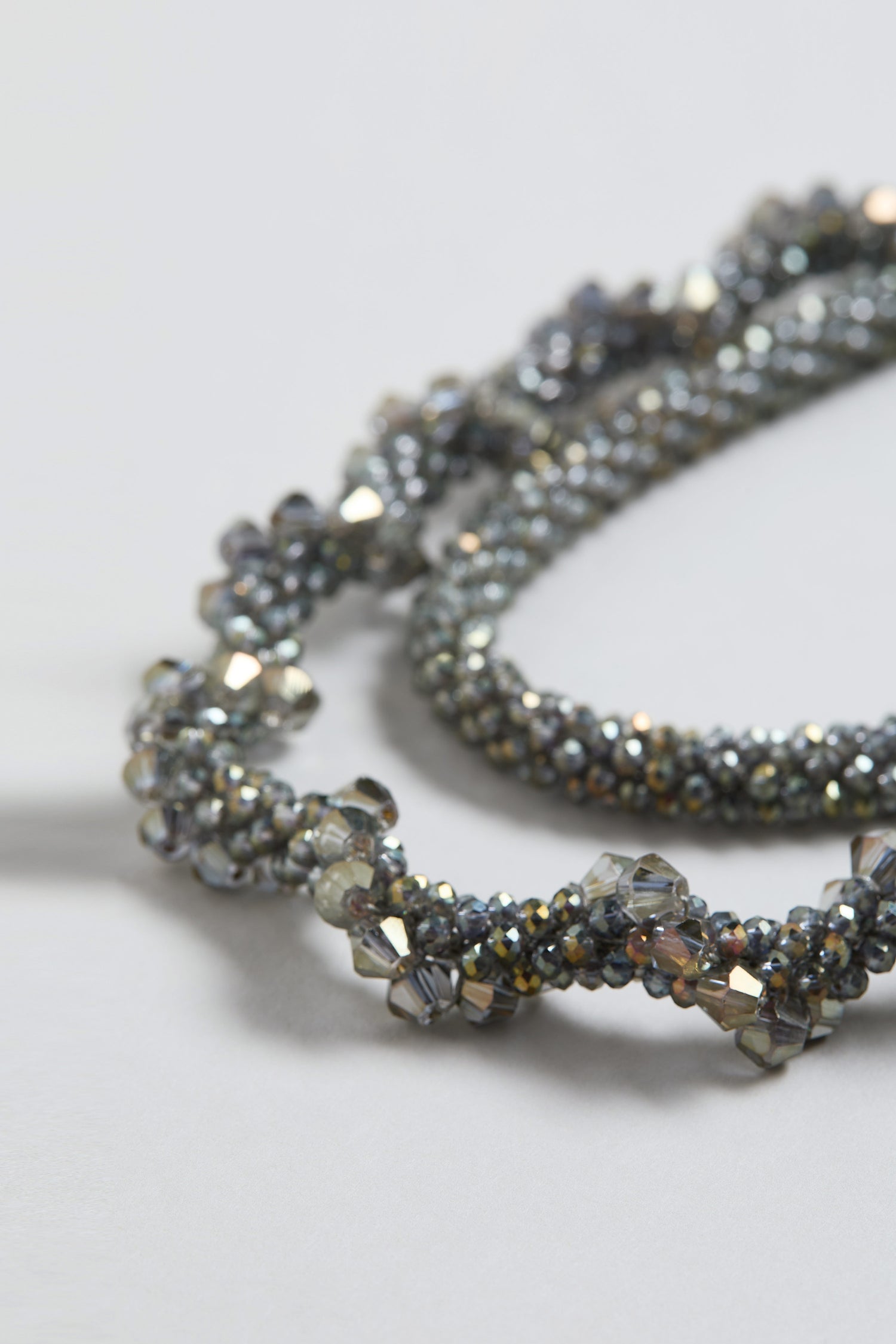Close-up of the Glacier Spiral Necklace, a silver piece with twisted metallic and glass beads in gradient gray and silver tones.