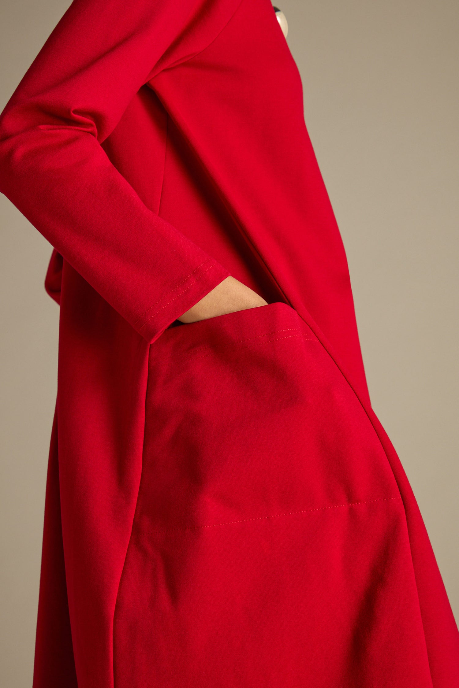A person wearing a red Ponte Pocket Dress with long sleeves and raglan armholes gently slips their hand into a side pocket.