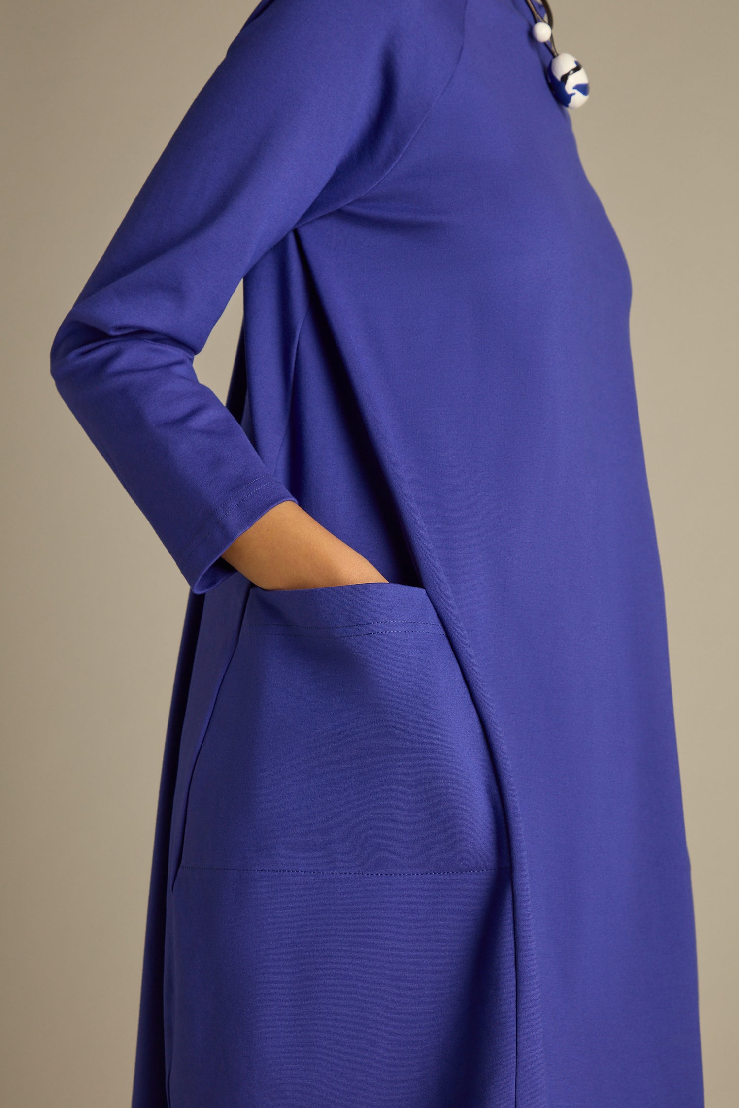 The individual is stylishly dressed in a blue Ponte Pocket Dress, which reaches calf length. Their hand rests casually in the side pocket, highlighting the dress's chic cocoon silhouette.