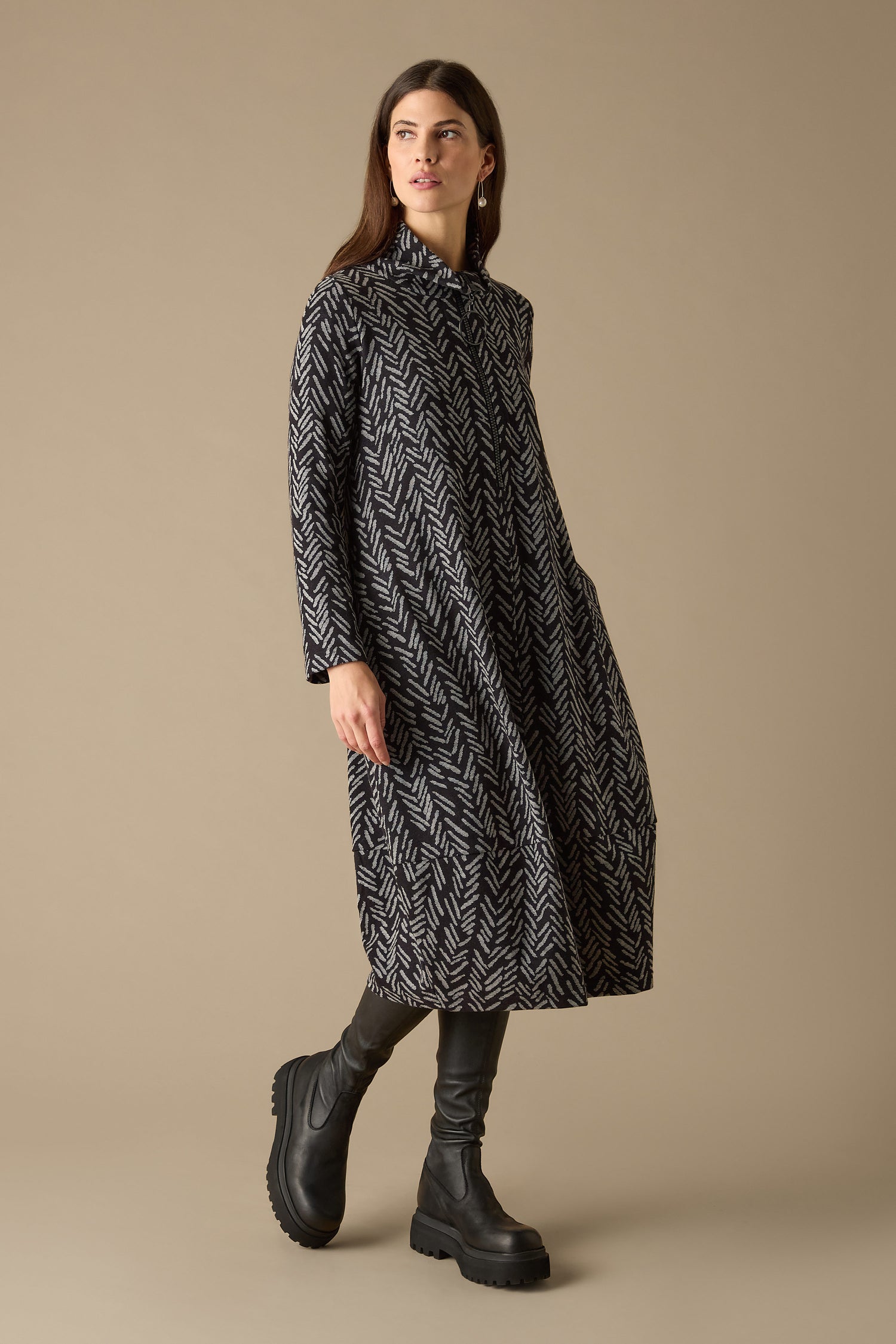 A person models a Herringbone Jersey Jacquard Dress over black leggings and chunky boots, standing against a plain beige background.