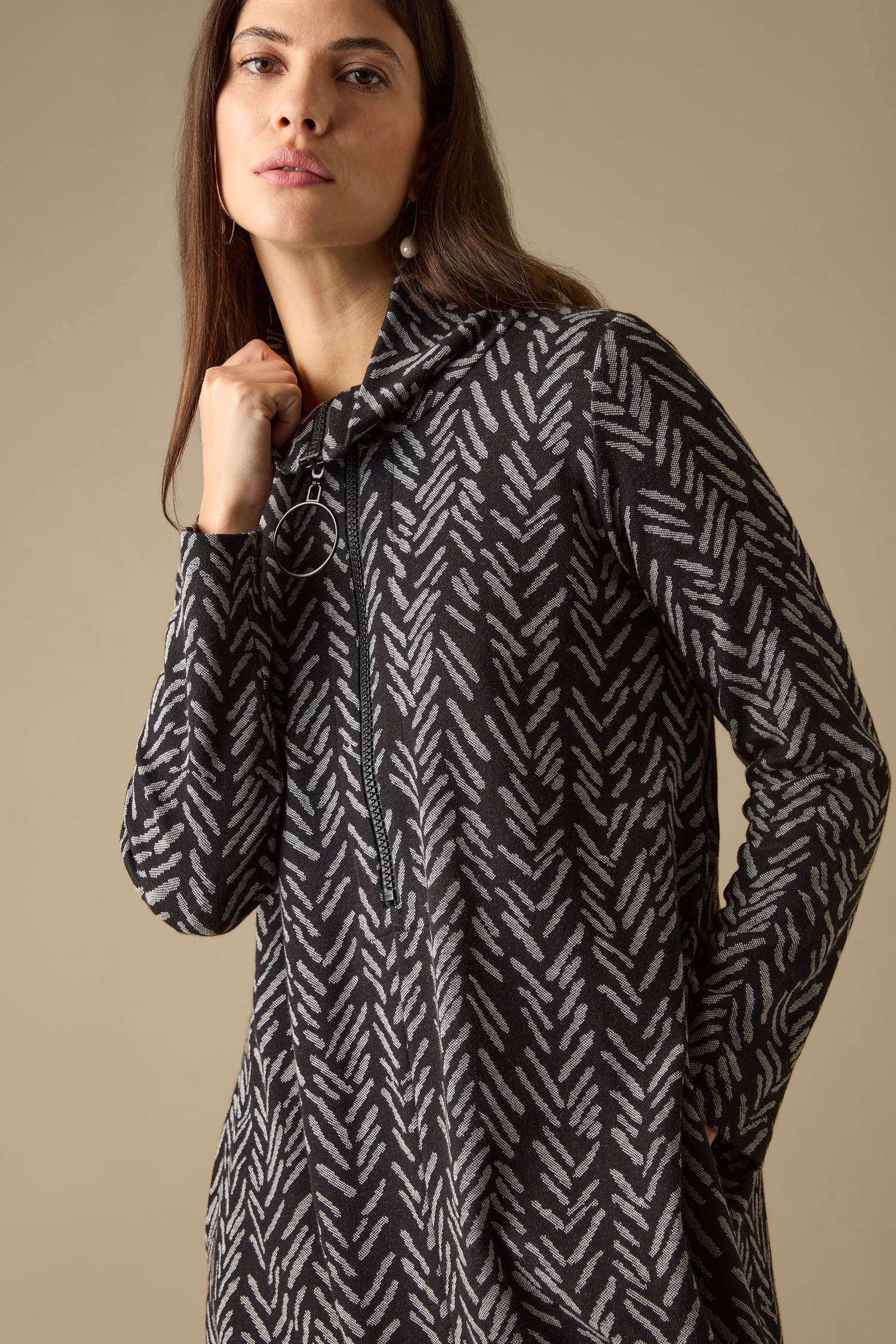 A person wearing a black and gray herringbone jersey jacquard fabric dress with a hood stands against a beige background.