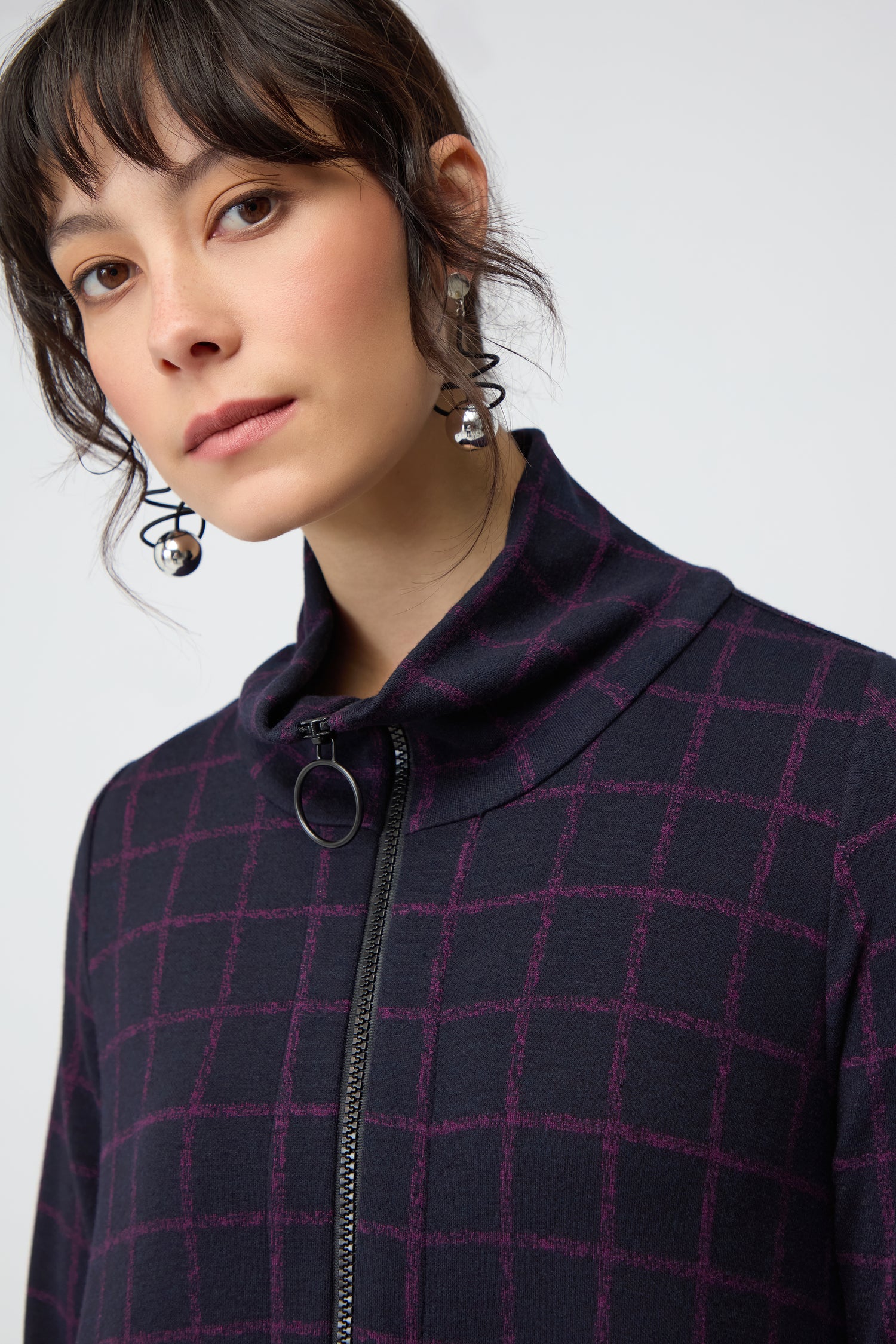 A woman wearing the Small Broken Check Zip Bubble Dress gazes at the camera, accessorized with large spherical earrings, against a plain background.