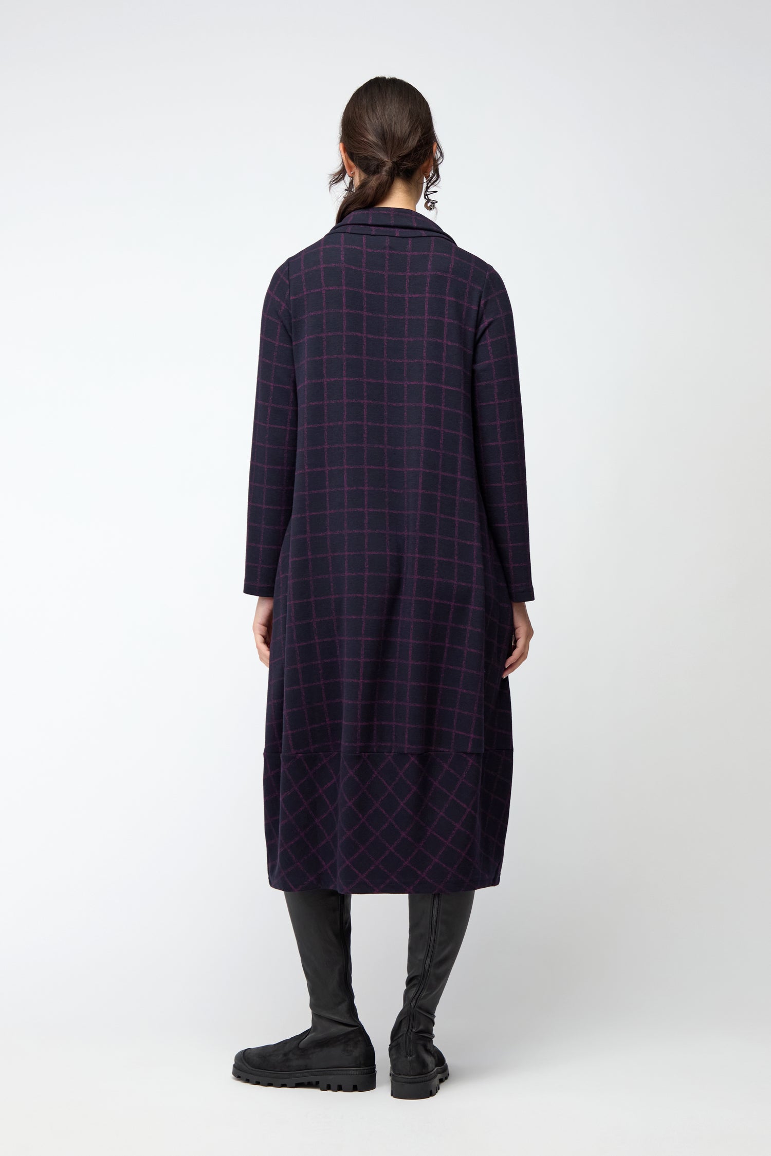 A person stands with back to camera, wearing the Small Broken Check Zip Bubble Dress in a dark check pattern and black boots against a plain white background.