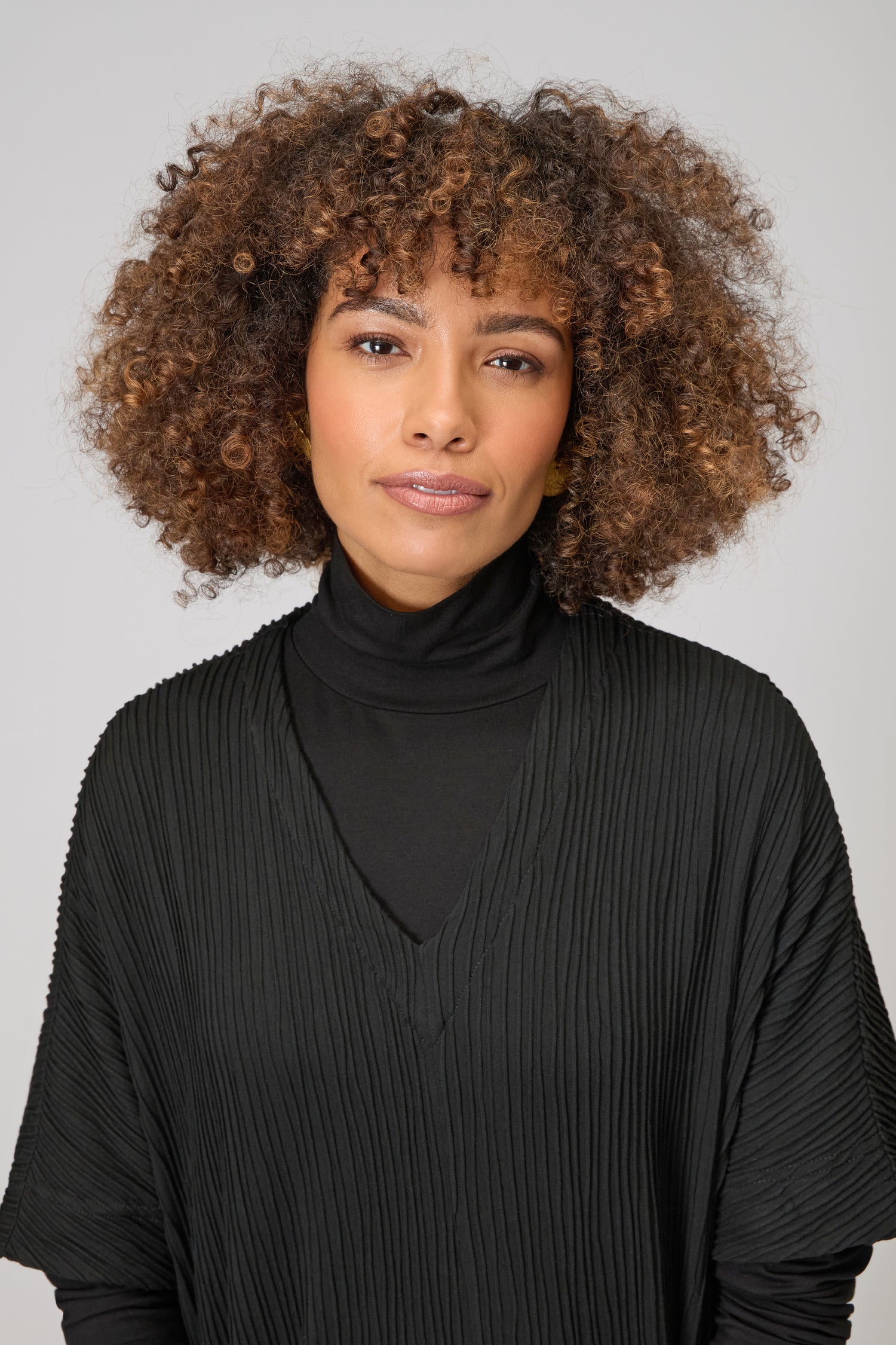 Woman with curly hair wearing the Textured Wave Jersey Dress, standing against a plain light background and looking at the camera with a neutral expression.