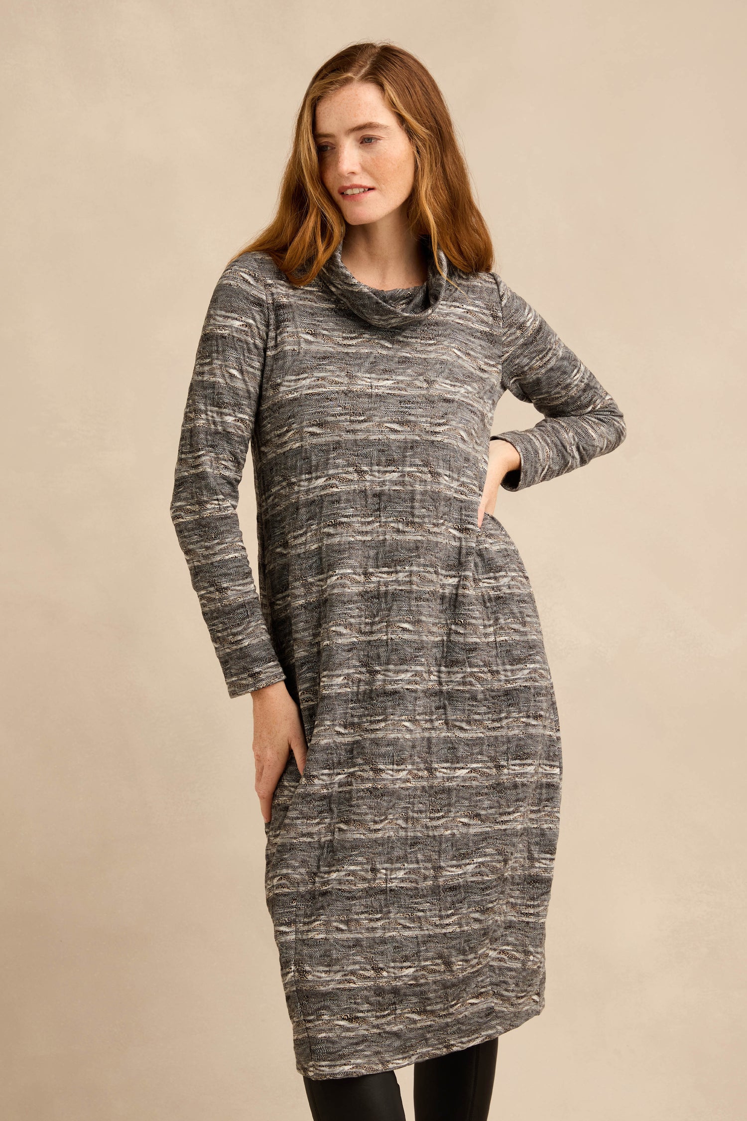 A woman stands with one hand on her hip against a neutral background, wearing the Abstract Ripple Jersey Bubble Dress—a long-sleeve, patterned gray textured dress featuring a cowl neck.