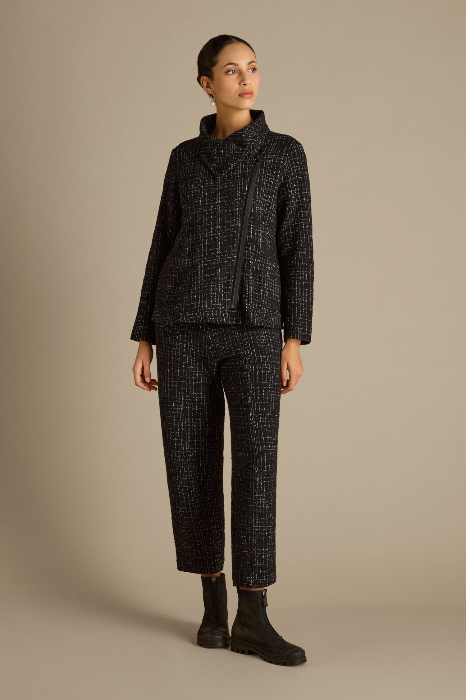 A person is wearing a Boucle Cotton Jersey Zip Jacket paired with textured black pants and matching boots, echoing a biker silhouette, standing against a beige background.