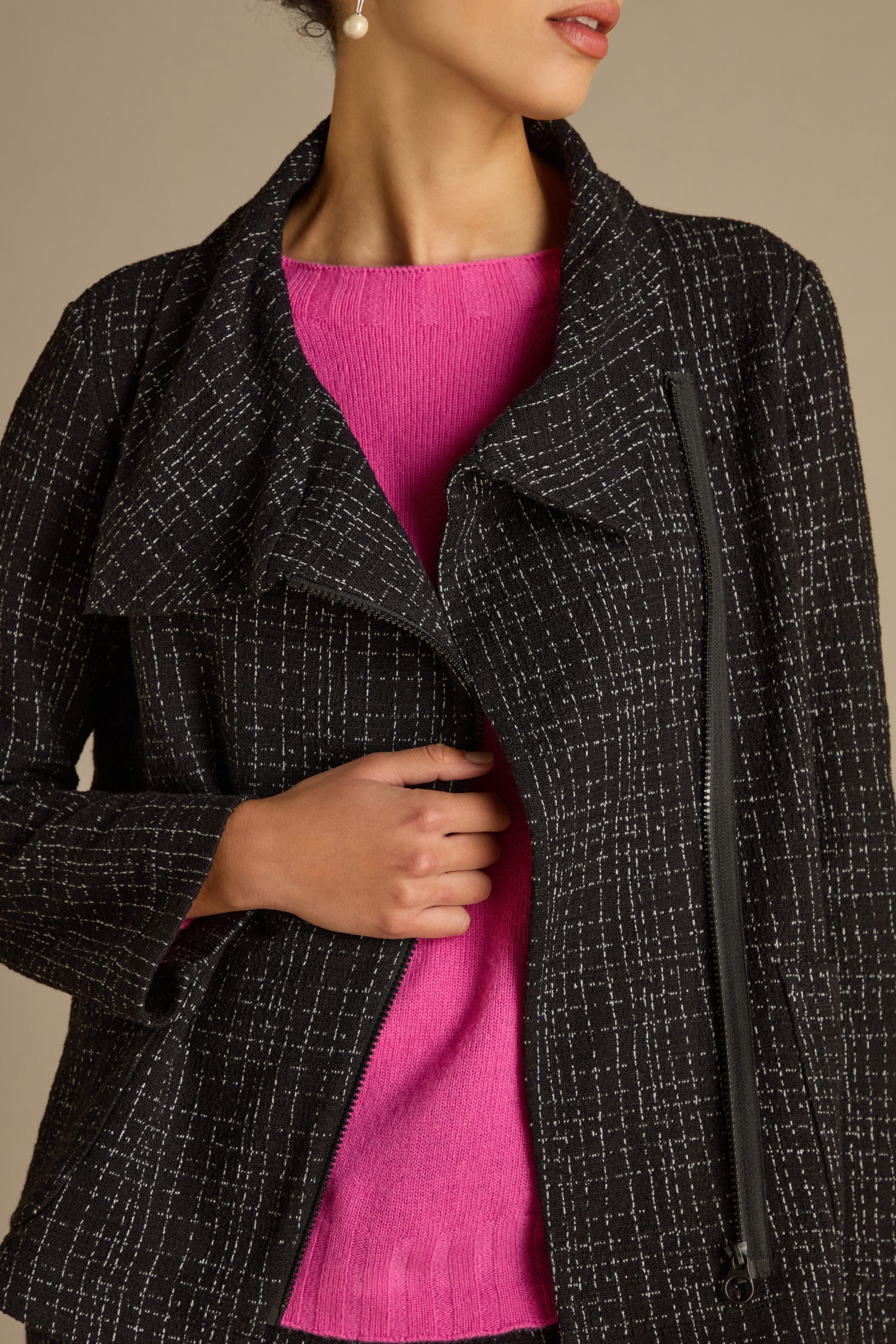 A person wearing the Boucle Cotton Jersey Zip Jacket in a black pattern over a pink top is adjusting it, highlighting its chic biker silhouette.