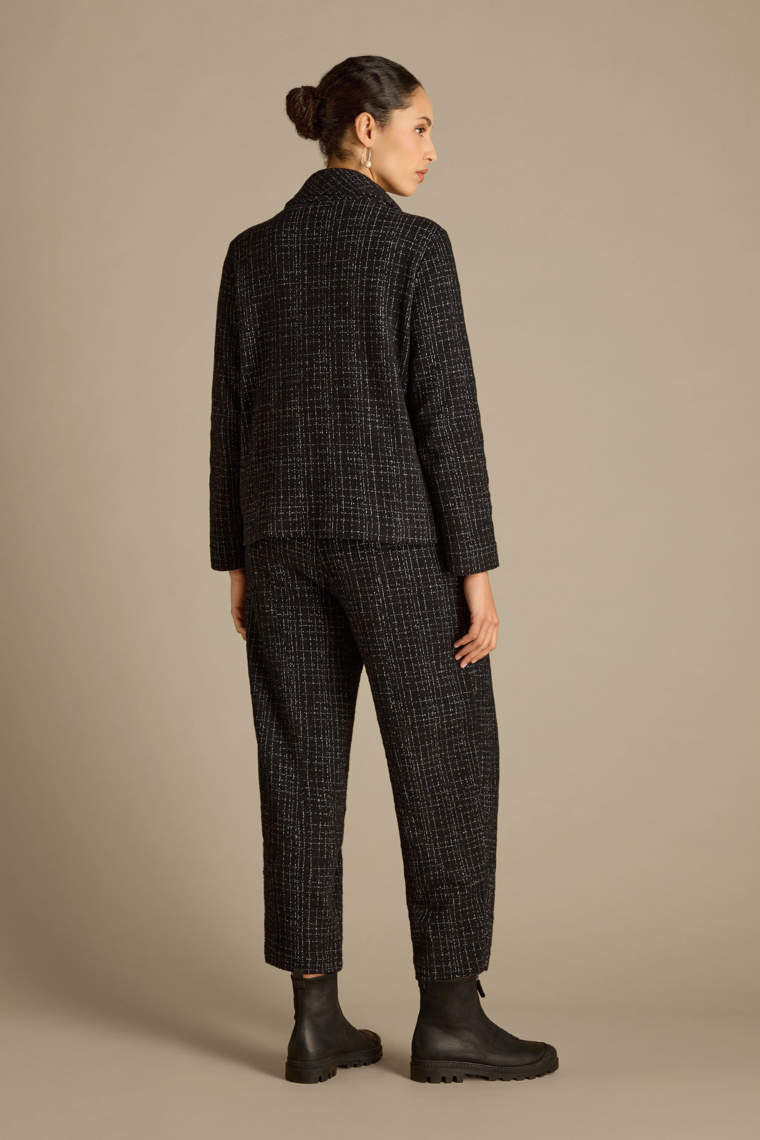 A person wearing a matching black textured pantsuit and boots, styled with the Boucle Cotton Jersey Zip Jacket that enhances the biker silhouette, stands in profile facing away from the camera against a plain background.