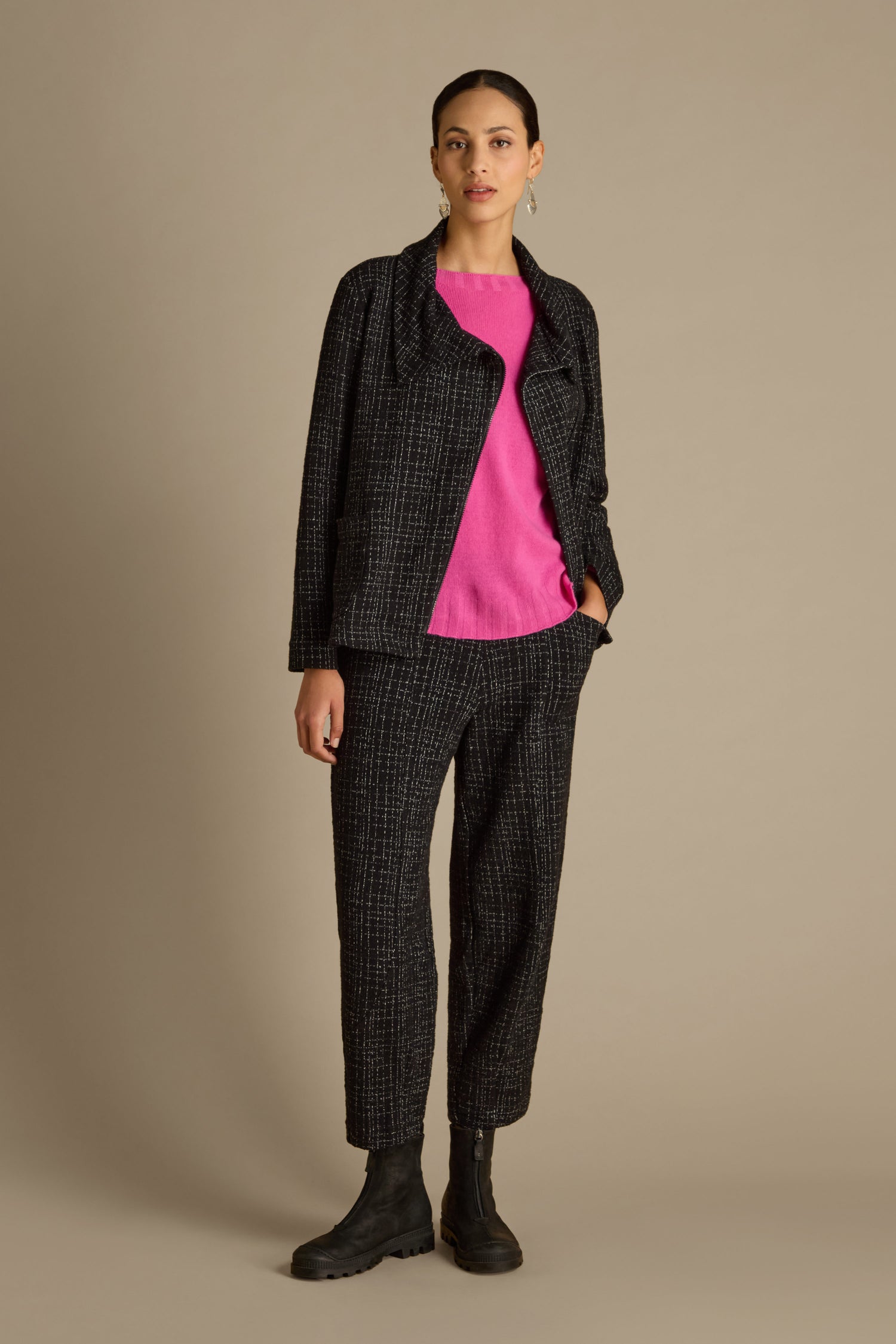 A person stands wearing the Boucle Cotton Jersey Zip Jacket, featuring a black speckled pattern and patch pockets, paired with a pink top and black boots against a plain background.