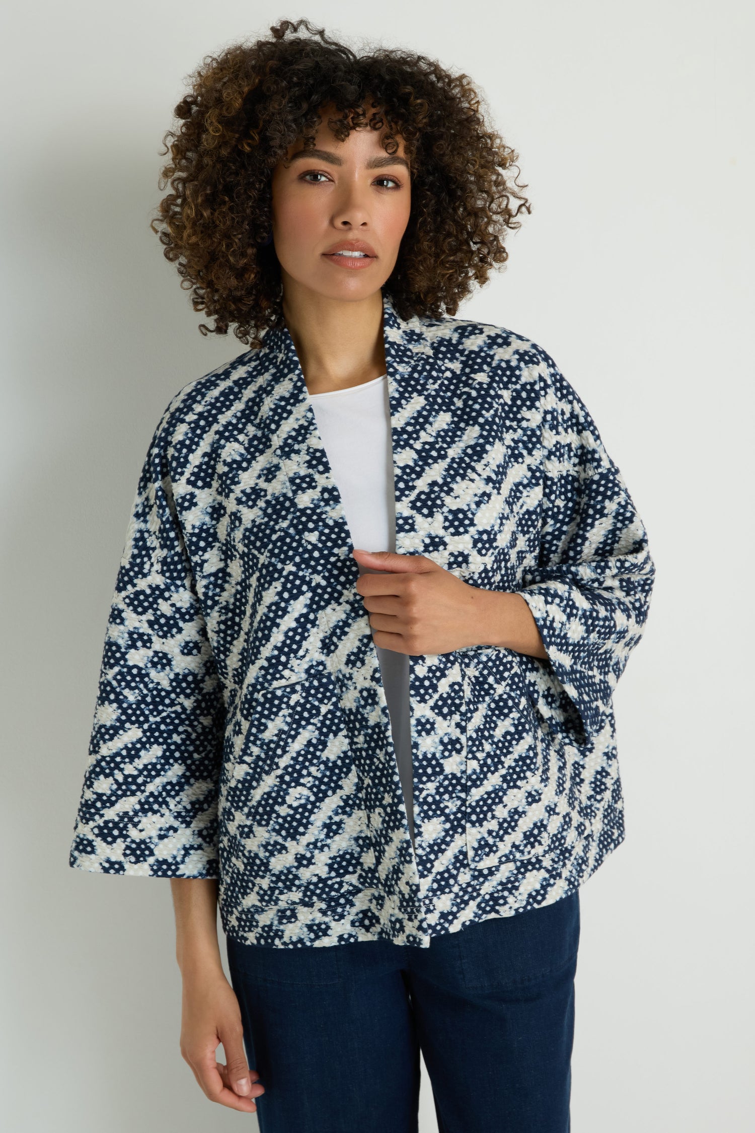 Wearing a Diamond Tie Dye Jersey Jacket styled like a kimono over a white shirt and dark pants, this person stands against a plain light background.