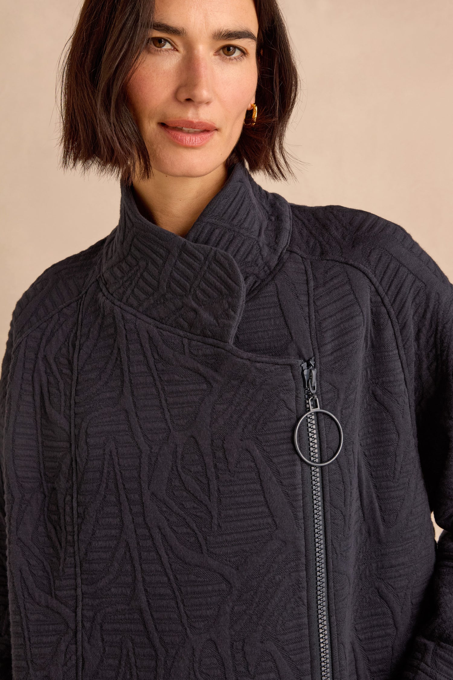A woman wearing the Quilted Zip Through Jacket, featuring a textured, cotton-rich design with an off-center zipper and high collar, stands against a neutral background.