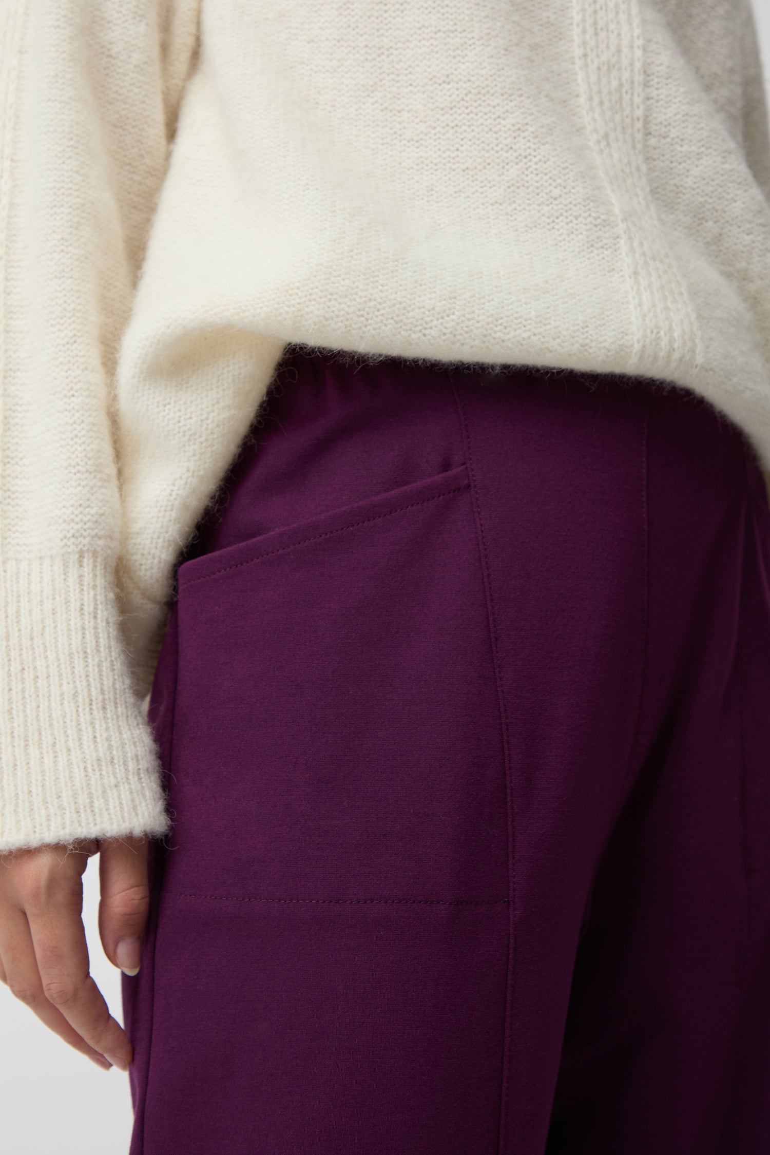 A person wears a cream knit sweater and purple Ponte Bubble Trousers, featuring an elasticated waistband and a visible side pocket, shown from the waist down.