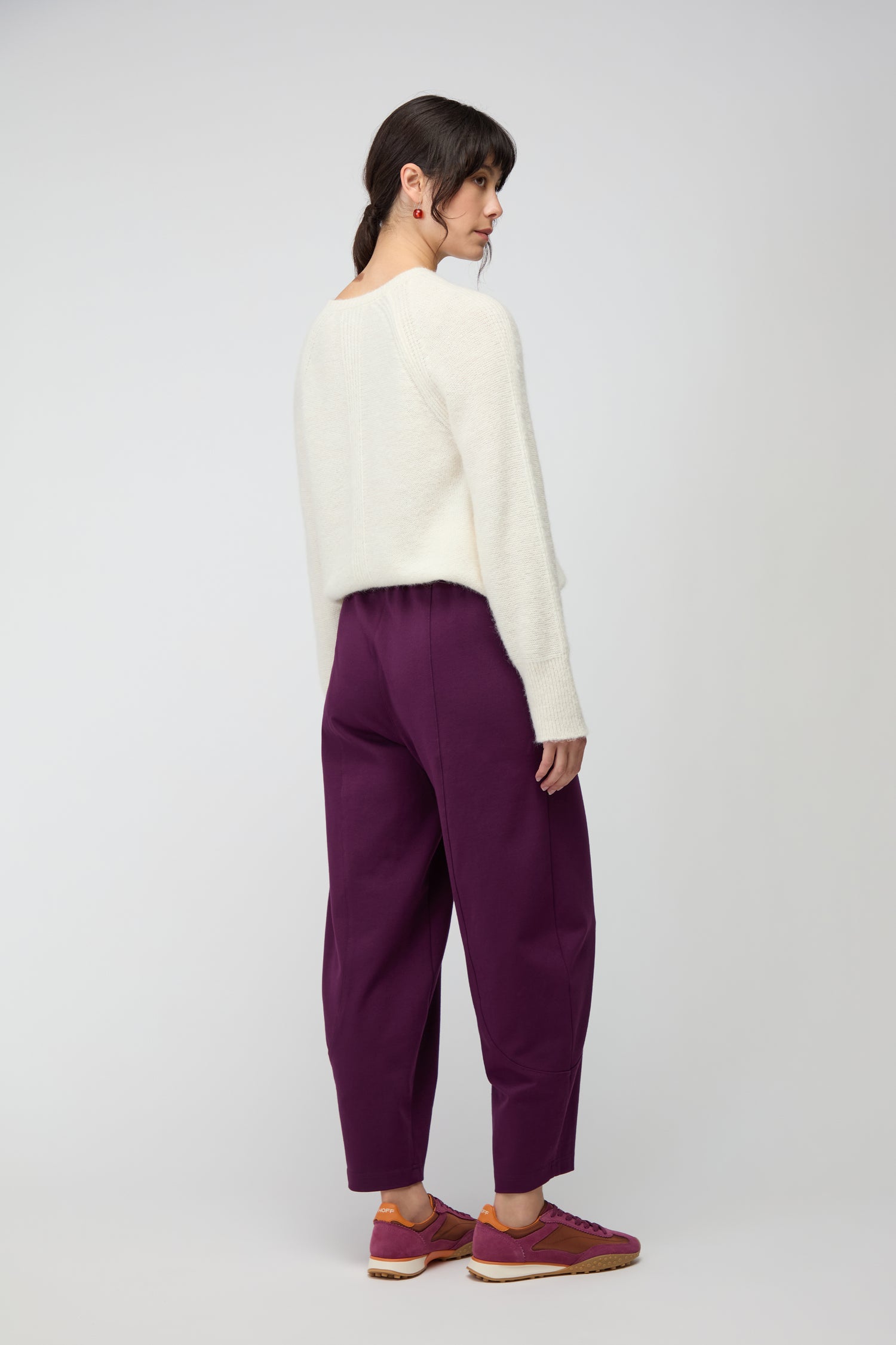 A person stands sideways, wearing a white sweater with Ponte Bubble Trousers and red sneakers, against a plain light background.