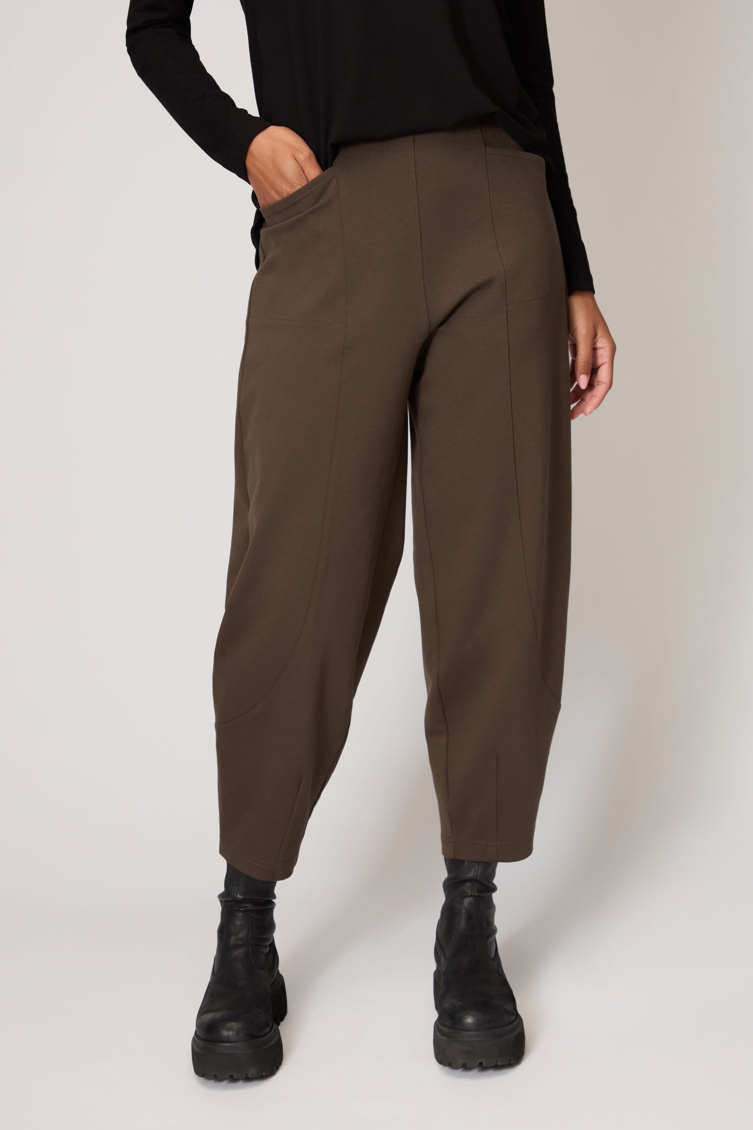 A person wears loose-fitting brown Ponte Bubble Trousers with an elasticated waistband, paired with a black long-sleeve top and black boots, standing against a plain light background.