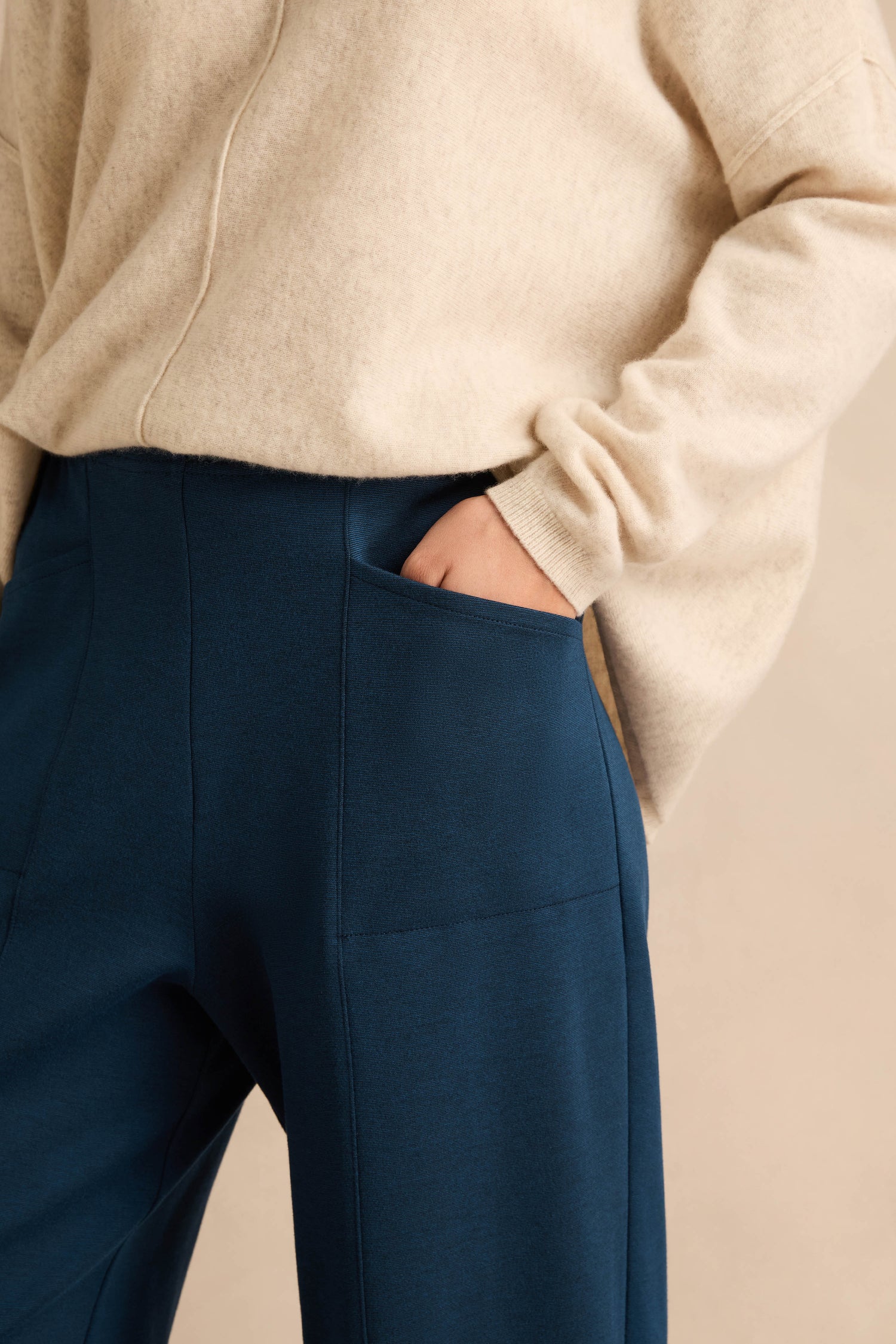 A person wearing a beige sweater and the Marine Ponte Bubble Trousers—dark blue with a rounded leg silhouette in soft ponte jersey—has their hand tucked into the pants pocket, shown from shoulder to mid-thigh.