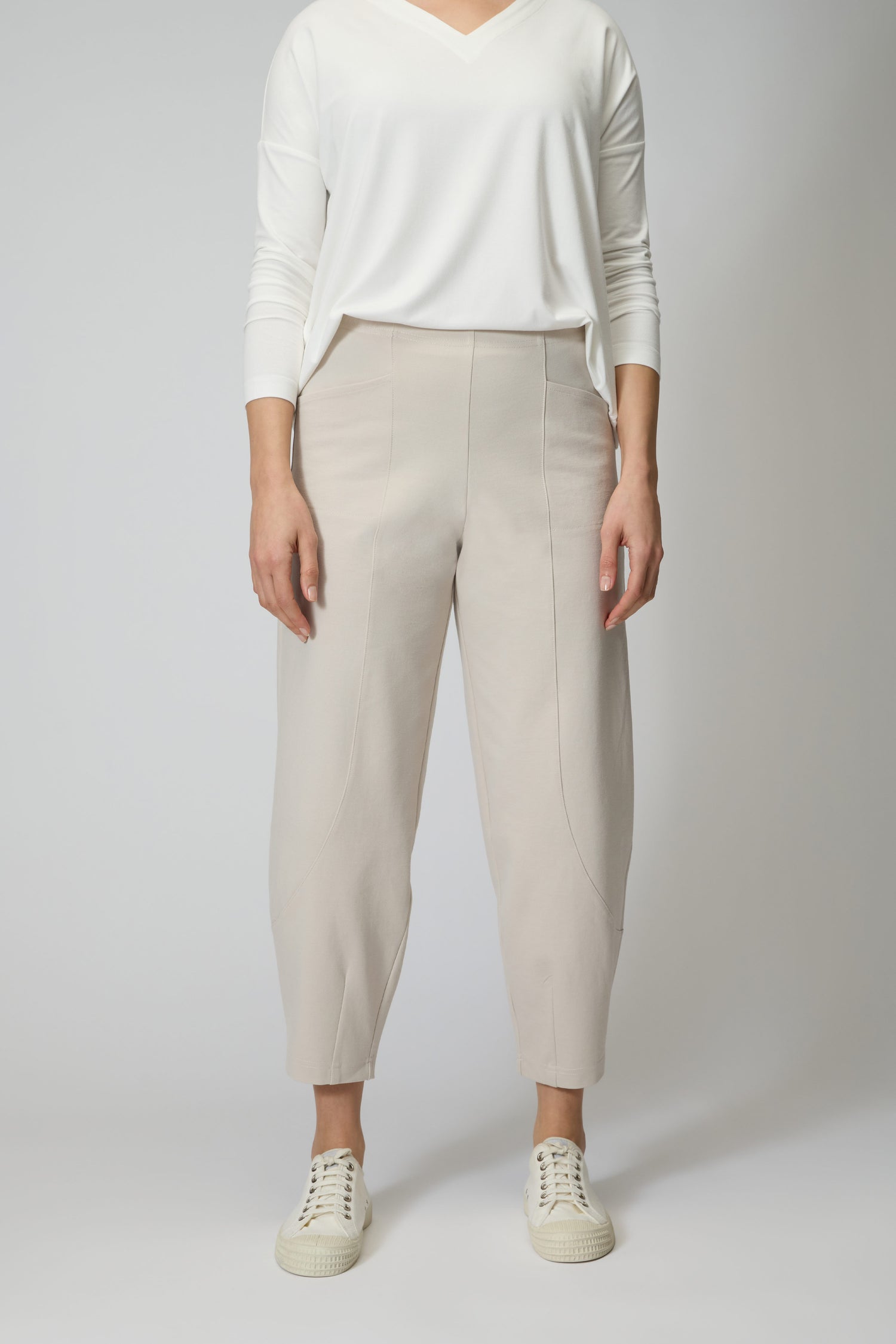 Person wearing a white long-sleeve top, Ecru Ponte Bubble Trouser with a bubble leg silhouette in light beige, and white sneakers, standing against a plain light background.