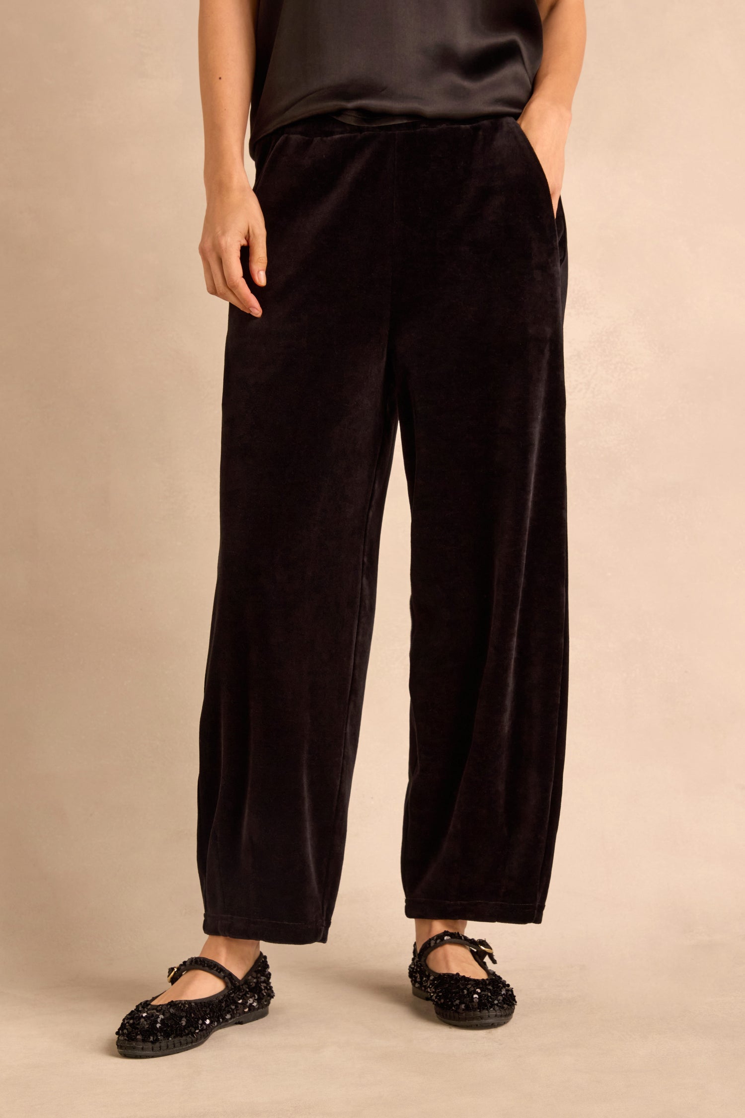 Wearing the Black Velvet Jersey Bubble Trousers in a relaxed, loose-fitting bubble silhouette, paired with a black top and black embellished flat shoes, the person stands against a neutral background.