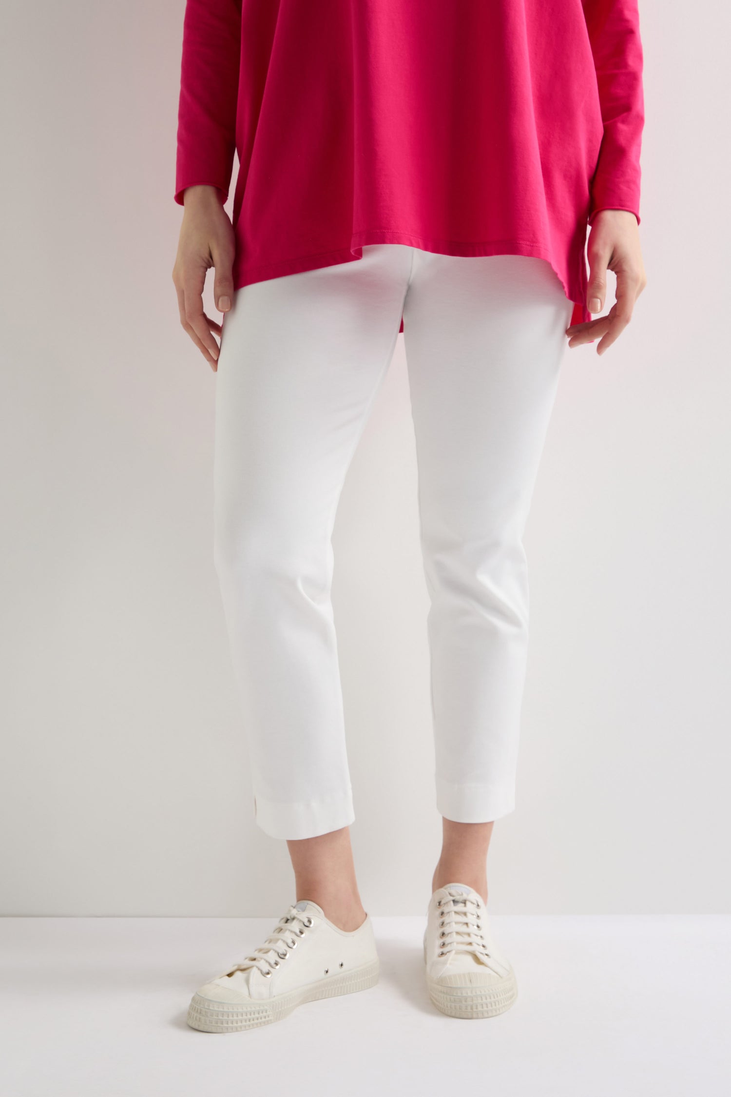 A person in a red top and white sneakers wears sleek Ponte Slim Leg Trousers with an elasticated waistband, standing against a pristine white backdrop.