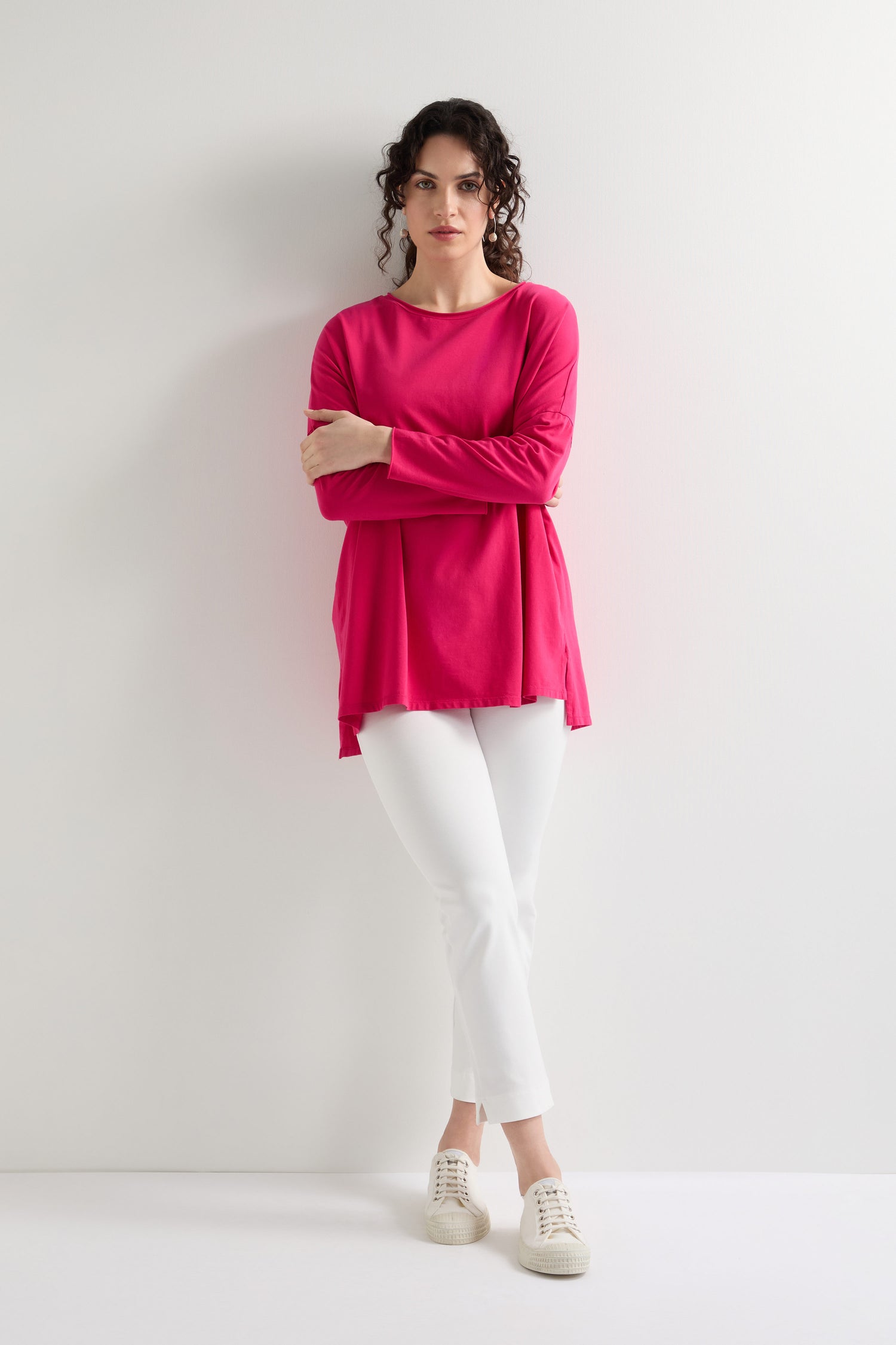 A person with curly hair is wearing a bright pink top and the Ponte Slim Leg Trouser, which features an elasticated waistband for comfort. The sleek silhouette of the white trousers enhances their style against the plain white background.