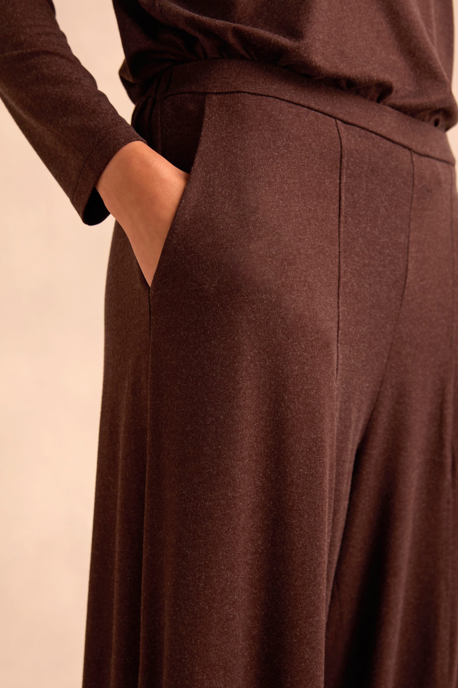 A person shown from waist to mid-thigh wears loose-fitting Soft Viscose Jersey Bubble Trousers in brown, with one hand in the pocket against a plain, neutral background.