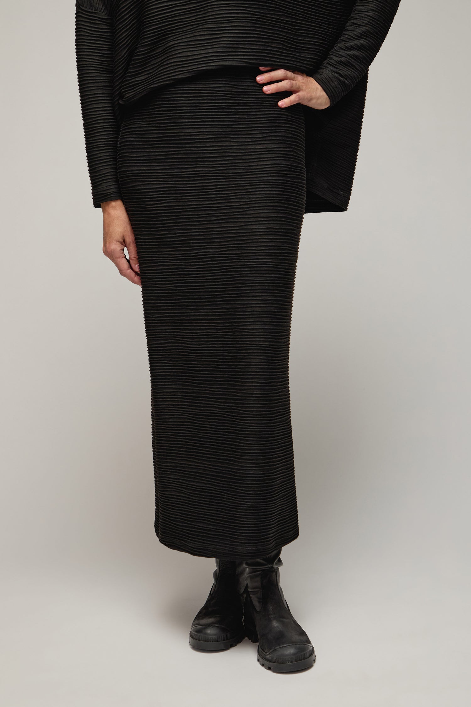 Person wearing a Textured Wave Jersey Tube Skirt with a matching top and black boots, standing confidently against a plain background, one hand on their hip.