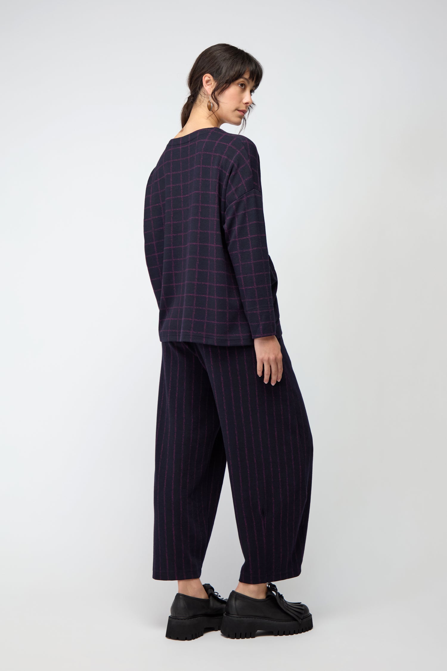 A woman stands in profile wearing the Small Broken Check & Stripe Boxy Top with matching wide-leg pants and black chunky shoes against a plain light background.
