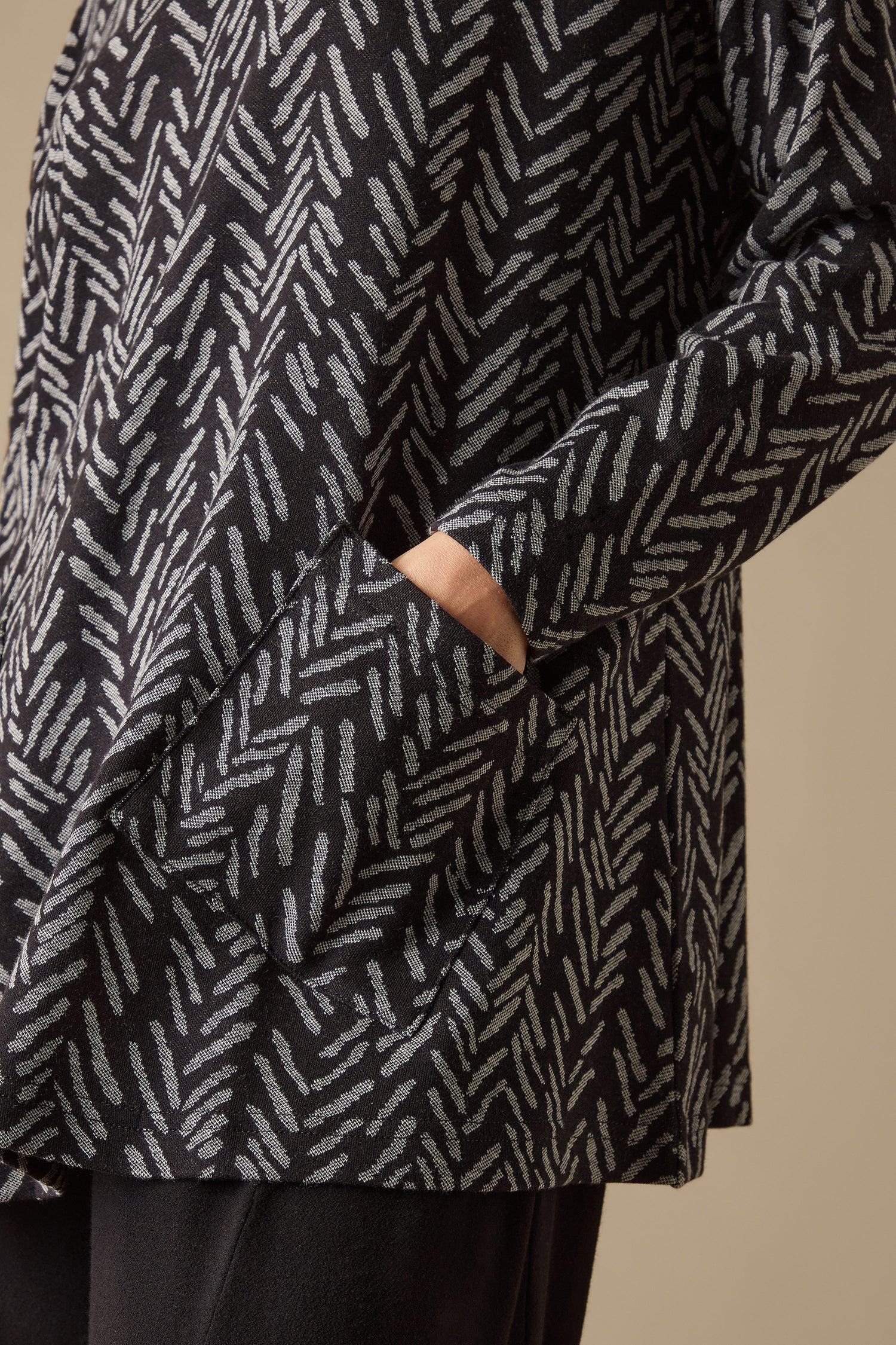 A person is sporting a Herringbone Jersey Jacquard Top featuring a black and gray pattern, complete with a funnel neck and boxy fit, with their hands casually resting in the pockets.