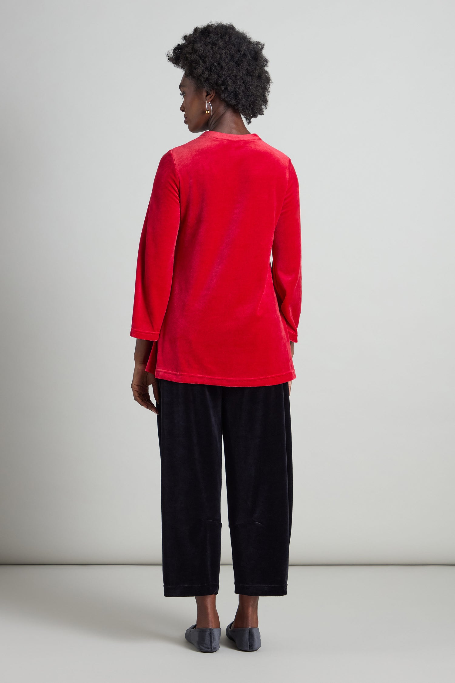 A person is shown from the back, dressed in a Velvet Jersey Horseshoe Neck Top in red, paired with black pants and gray shoes, set against a plain background.